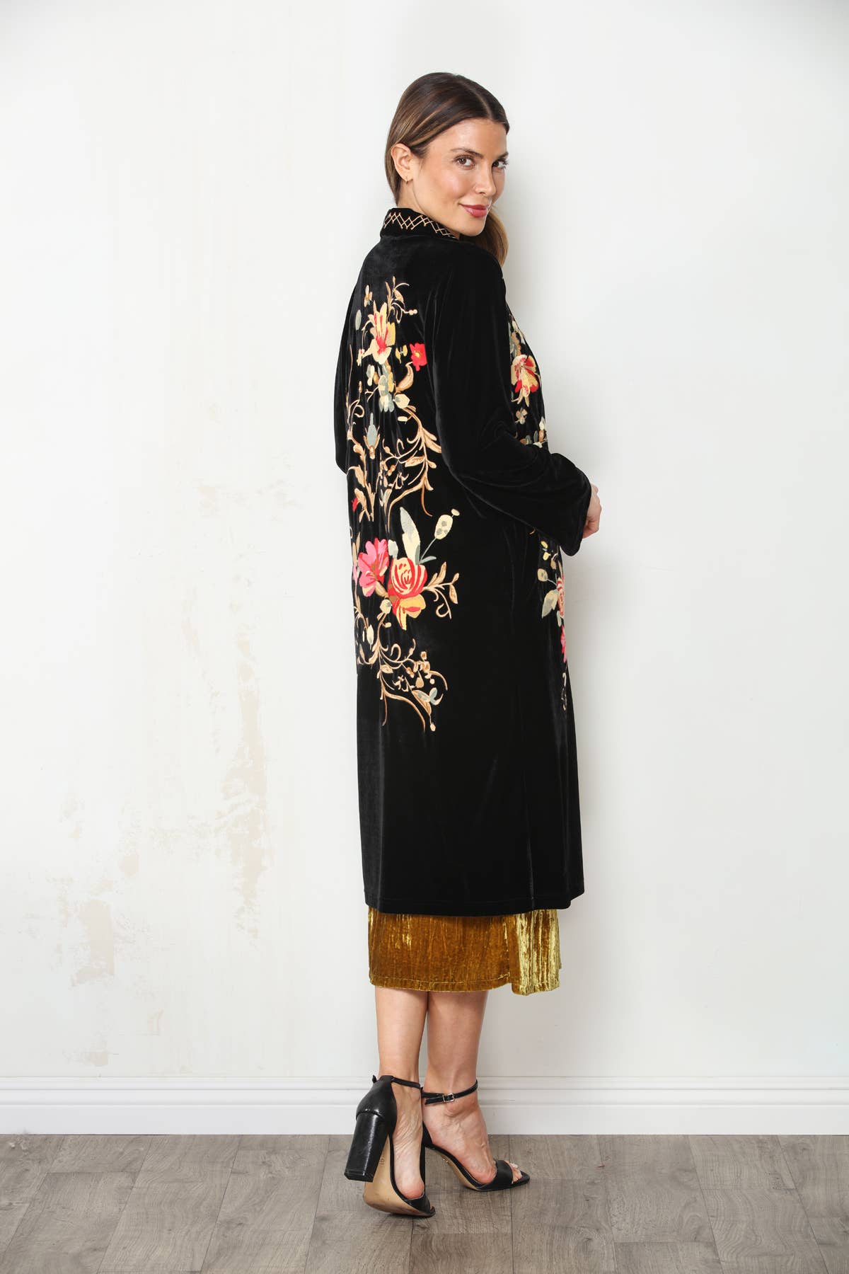 Three-quarter back view of black velvet duster showing colorful floral vine embroidery and long straight silhouette.