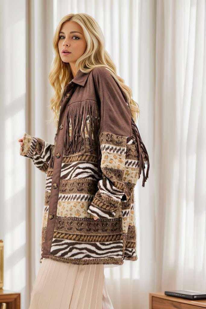 Side view of brown Aztec print shacket with fringe detailing across the chest and back, button-front closure, and long sleeves, styled with cream pleated pants.