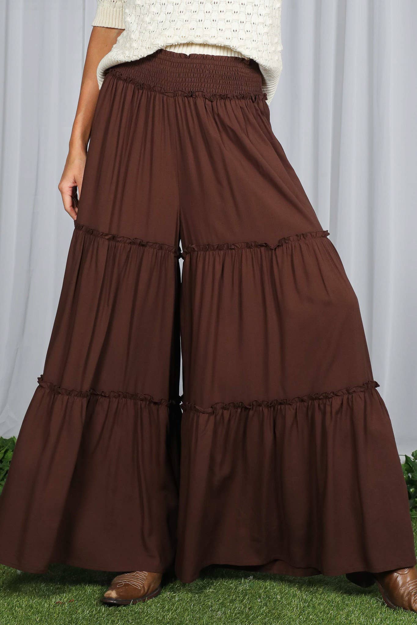 Woman wearing tiered palazzo pants with smocked waistband in mocha and black, styled for fall with sweater and boots.