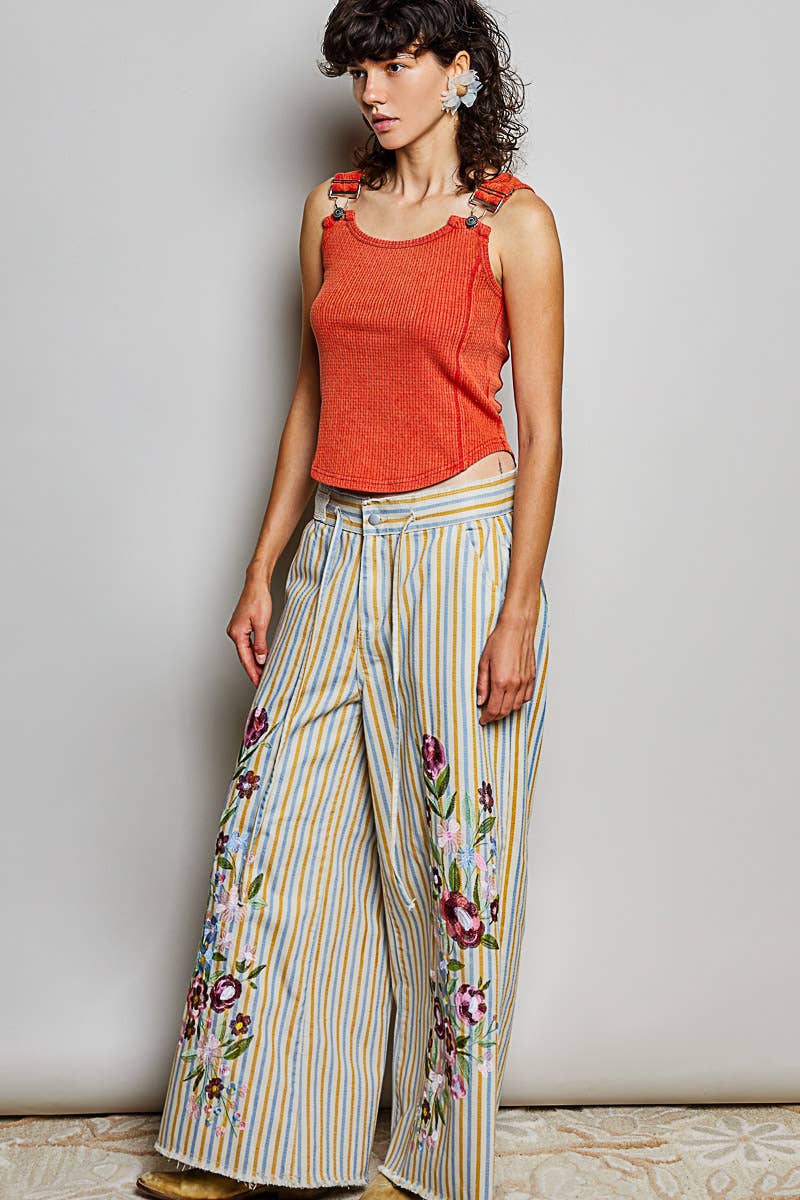 Model in an angled pose wearing Marigold Revival mustard and blue striped embroidered jeans with a coral tank