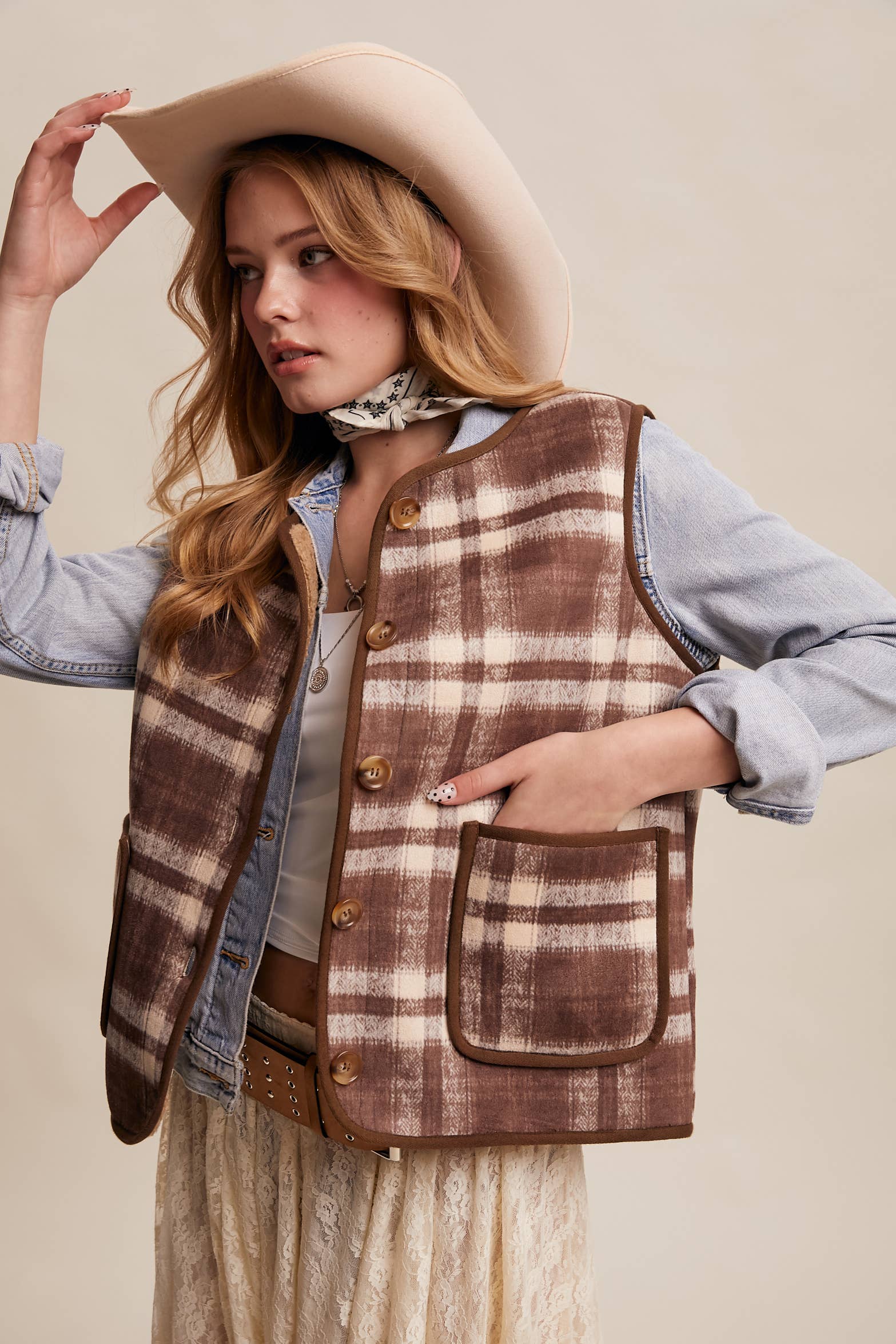 Woman wearing a plaid vest and cowboy hat on a beige background
