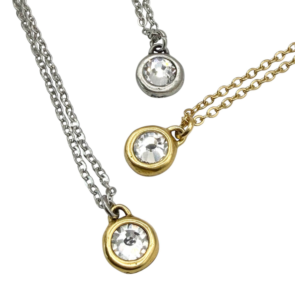 Two round bezel-set pendant necklaces on chains, one silver-tone and one gold-tone, each featuring a clear faceted gemstone, shown on a white background.