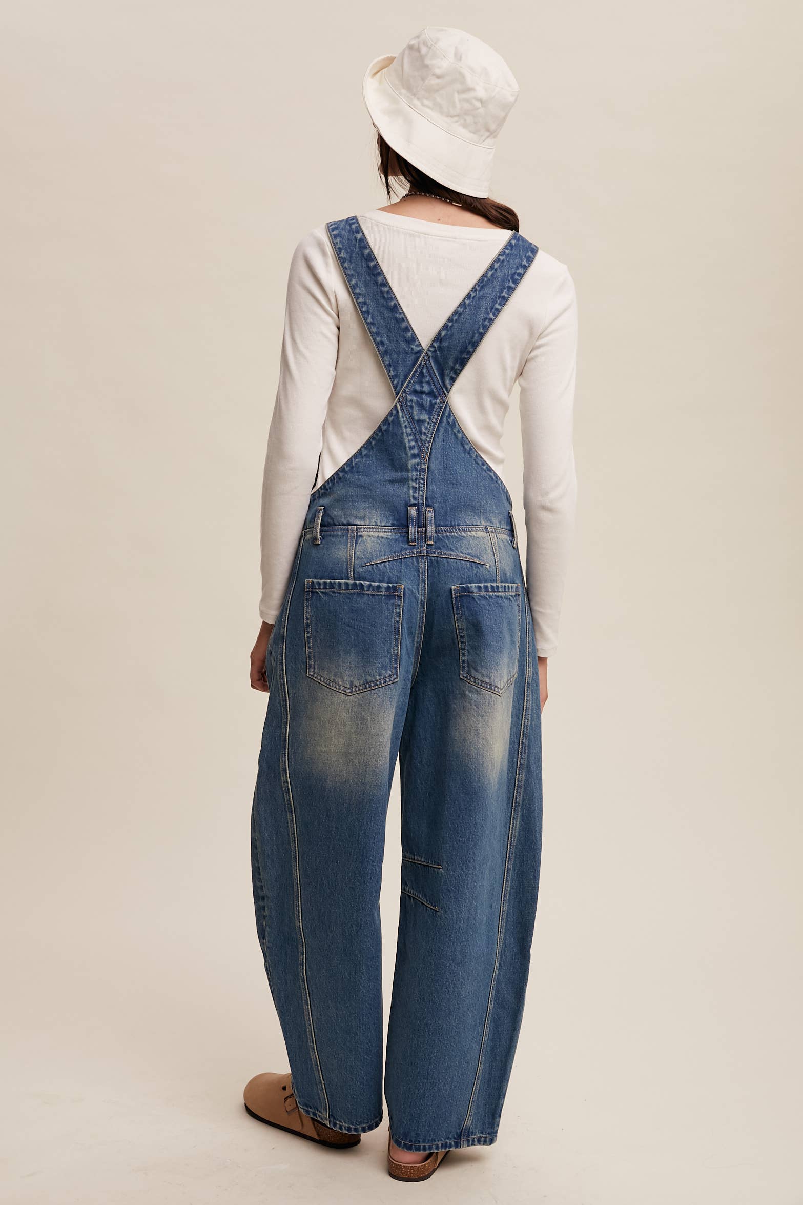 Back view- Side view- Vintage-inspired blue denim overalls with relaxed wide-leg fit, front chest pocket, and adjustable straps, styled with a white long-sleeve top and neutral clogs.