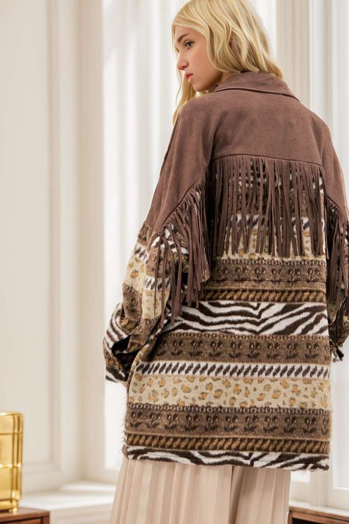 Back view of brown Aztec print shacket with fringe detailing across the chest and back, button-front closure, and long sleeves, styled with cream pleated pants.