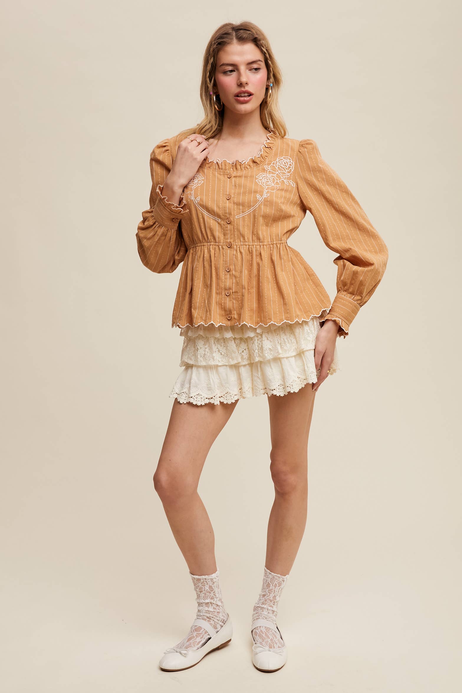 Side view- Camel pinstripe blouse with ruffled neckline, white rose embroidery, puff long sleeves, button front, and scalloped peplum hem—styled with white lace shorts.