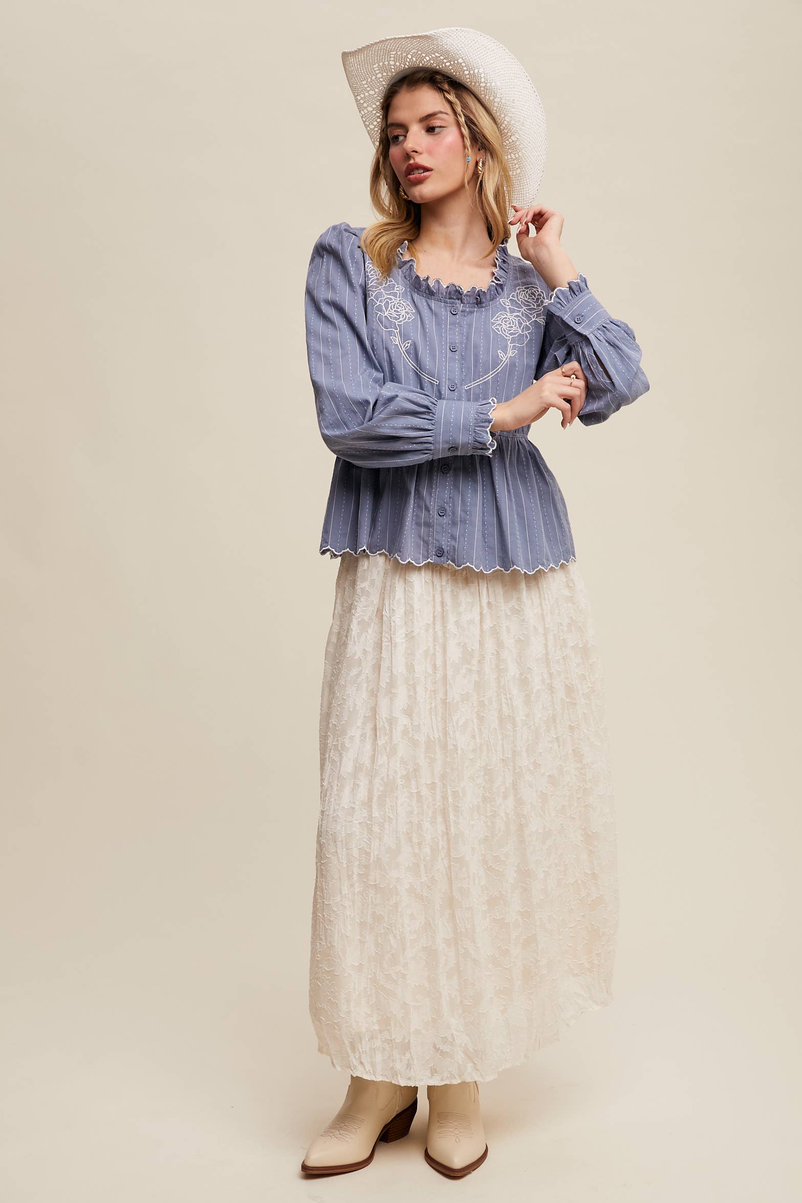 Dusty blue pinstripe blouse with ruffled neckline, white rose embroidery, puff long sleeves, button front, and scalloped peplum hem—styled with a white lace skirt and cowboy hat.