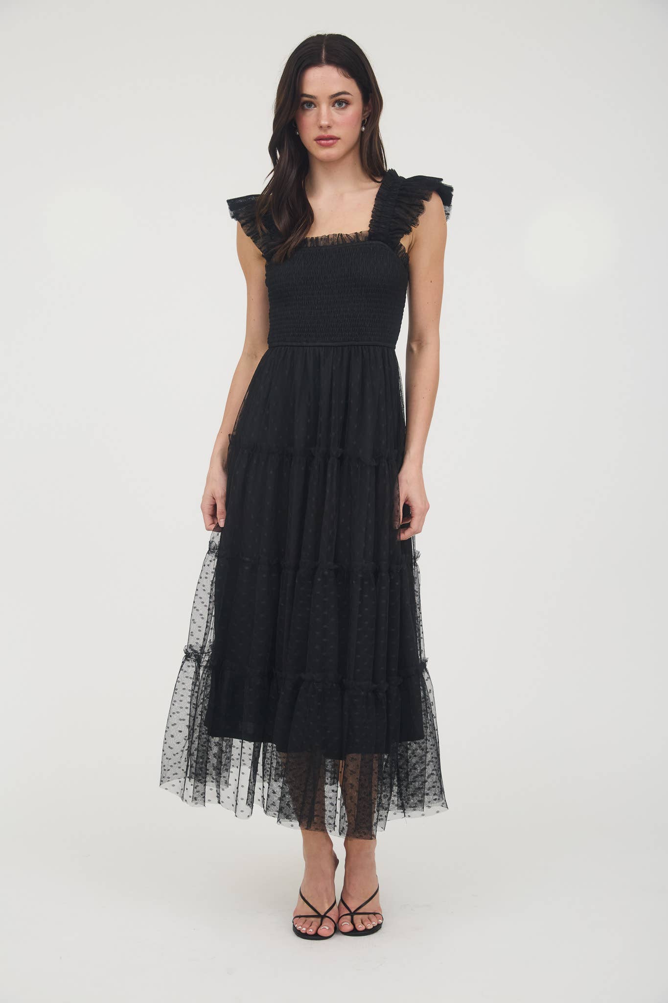 Model wearing black smocked midi dress with ruffle sleeves, tiered dotted mesh overlay, and flowy A-line silhouette.