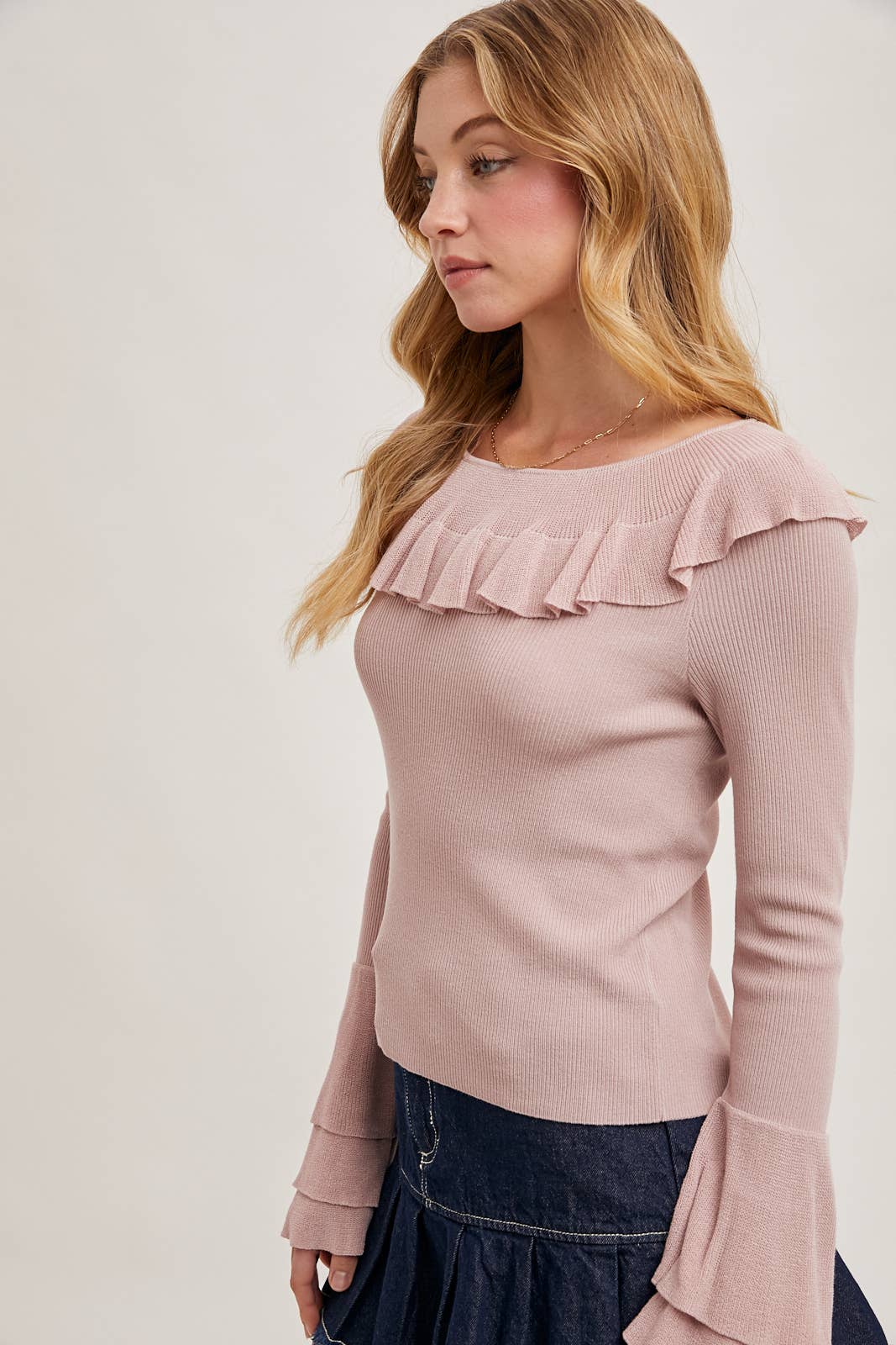 Rose ribbed knit sweater with ruffle neckline and tiered bell sleeves, paired with a dark denim skirt.