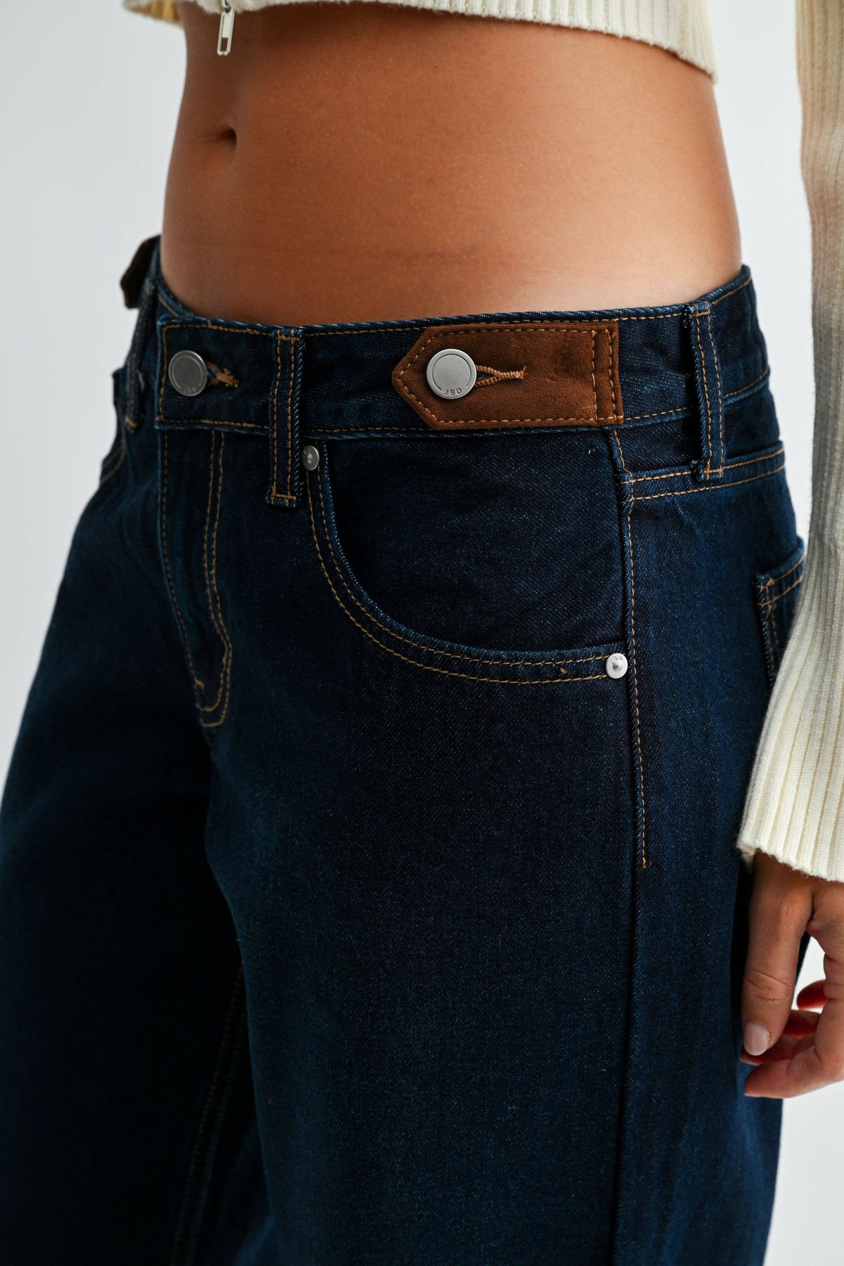 Close-up of Midnight Edge Cuffed Jeans showing a brown waistband tab with a silver-tone button and contrast pocket stitching