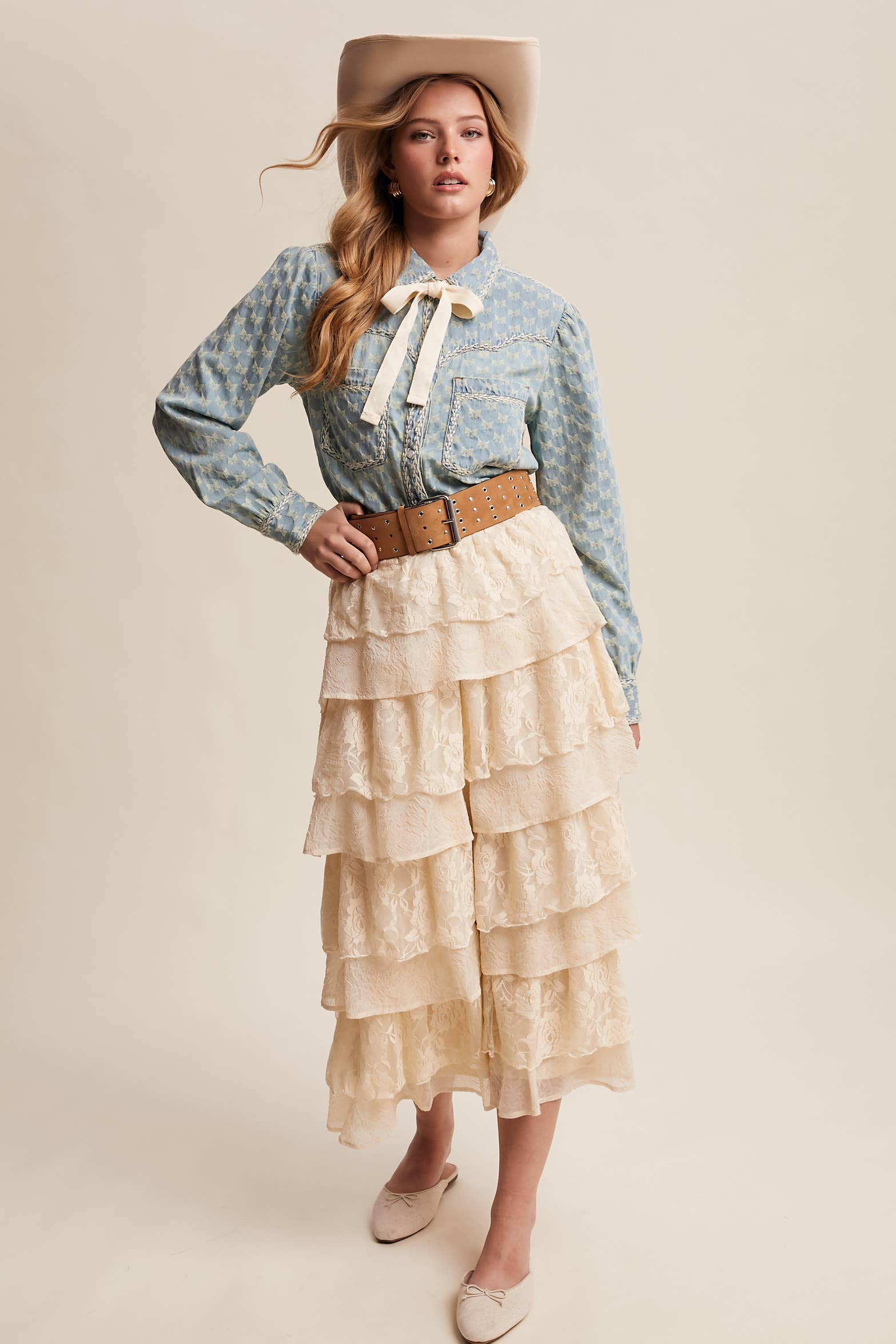 Light-wash denim blouse with cream bow-tie collar, tonal mini-bow pattern, braided contrast stitching, snap front, and two chest pockets.