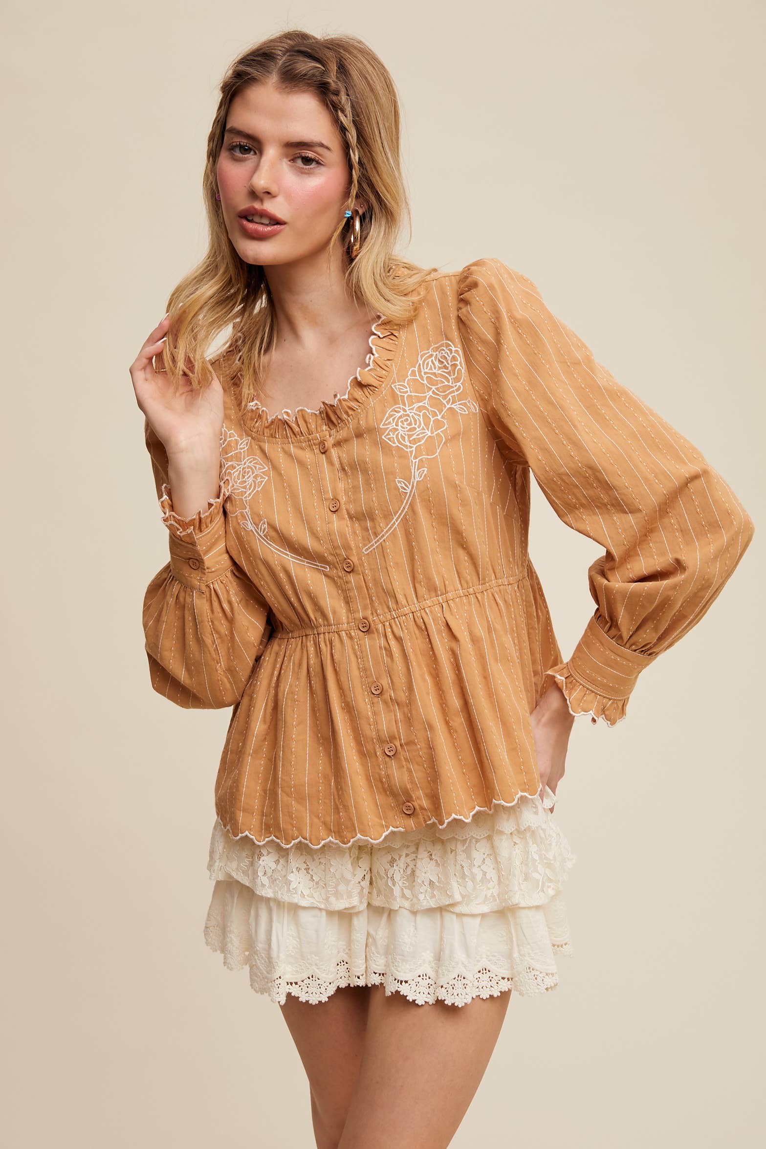 Camel pinstripe blouse with ruffled neckline, white rose embroidery, puff long sleeves, button front, and scalloped peplum hem—styled with white lace shorts.