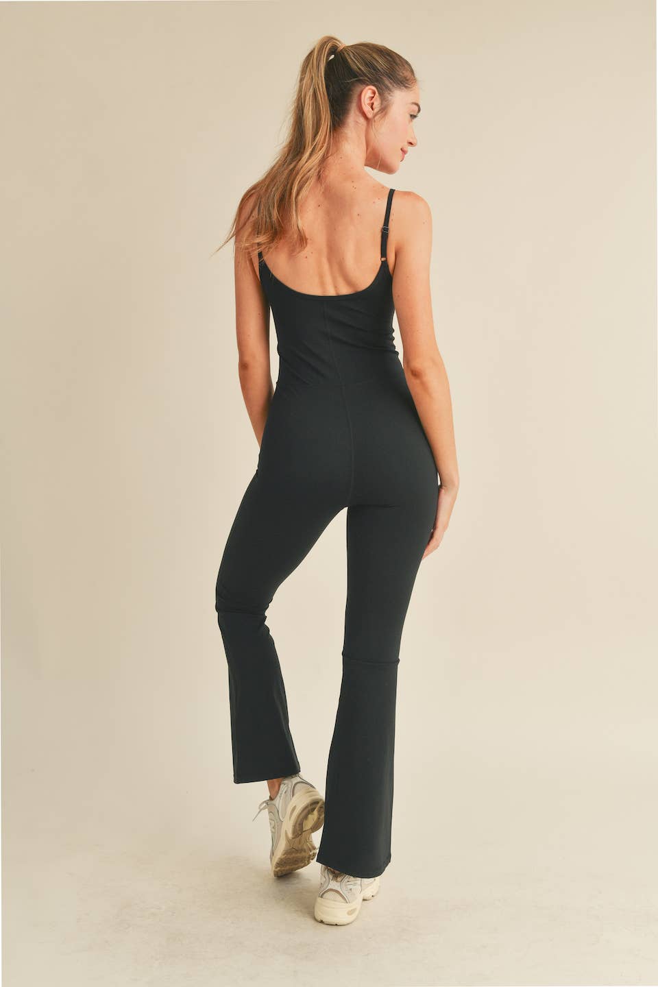 Rear view of Woman wearing Kimberly C flare jumpsuit in black with scoop neckline and flared leg.