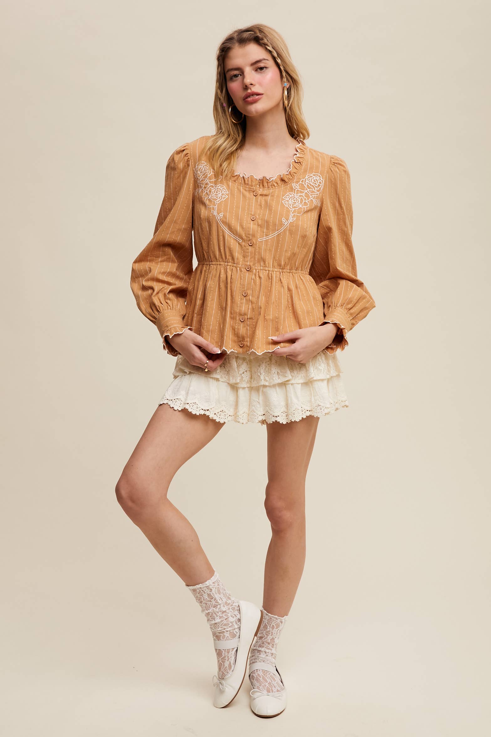 Side view- Camel pinstripe blouse with ruffled neckline, white rose embroidery, puff long sleeves, button front, and scalloped peplum hem—styled with white lace shorts.