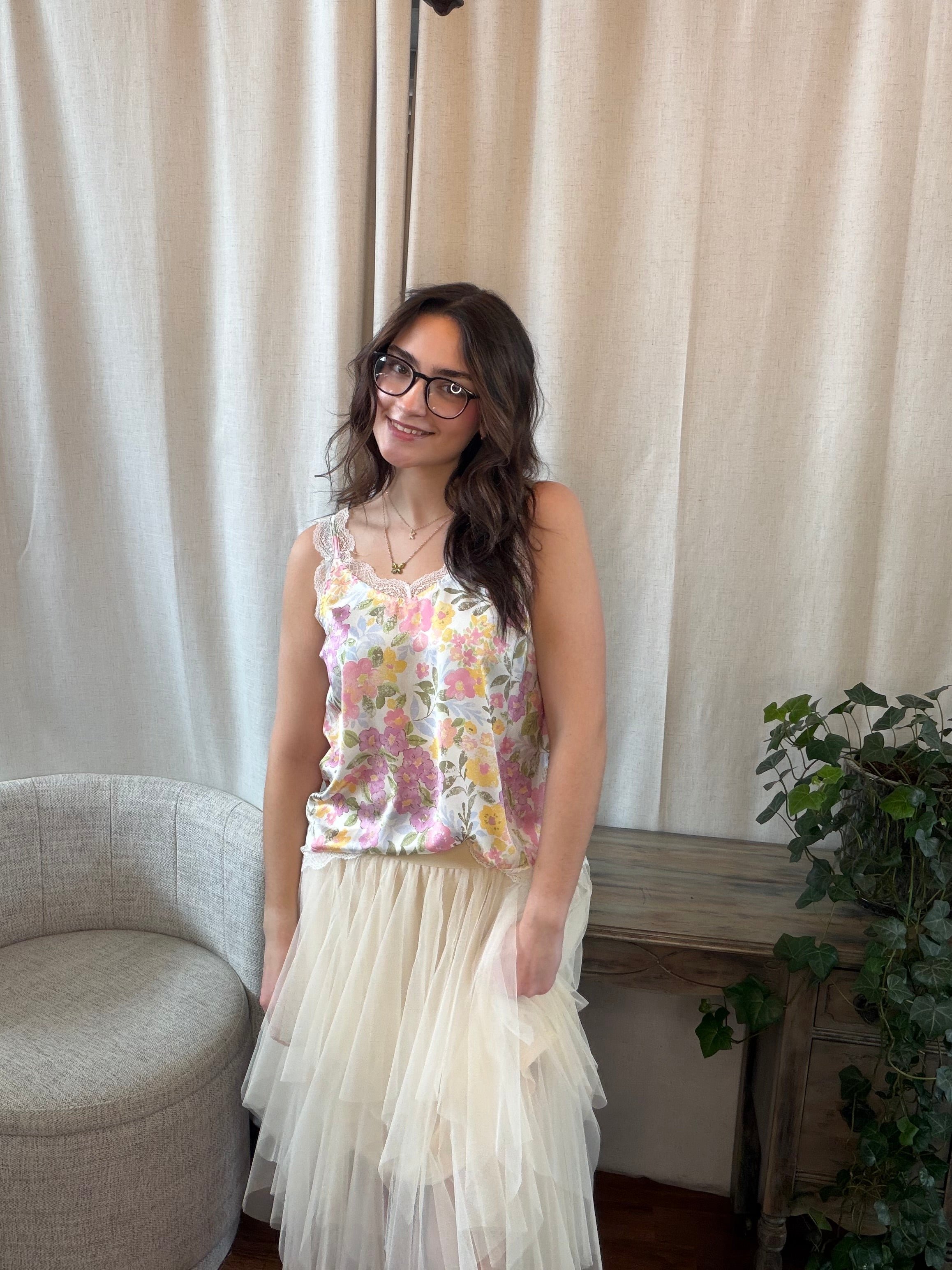 Woman wearing a floral top and tulle skirt standing in a room with a white curtain and plant.