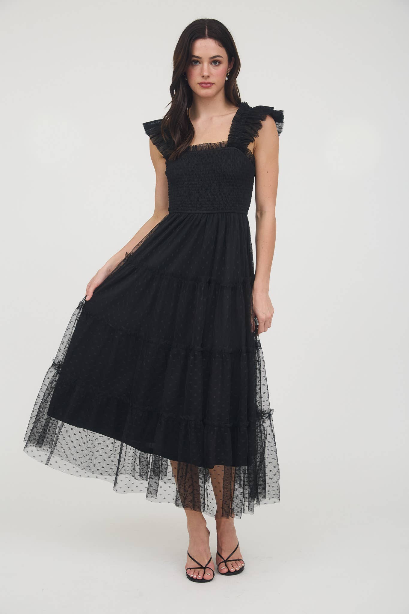 Model wearing black smocked midi dress with ruffle sleeves, tiered dotted mesh overlay, and flowy A-line silhouette.