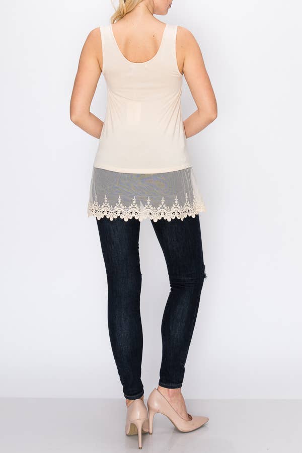 Woman wearing a beige tank top with lace trim and dark jeans on a white background