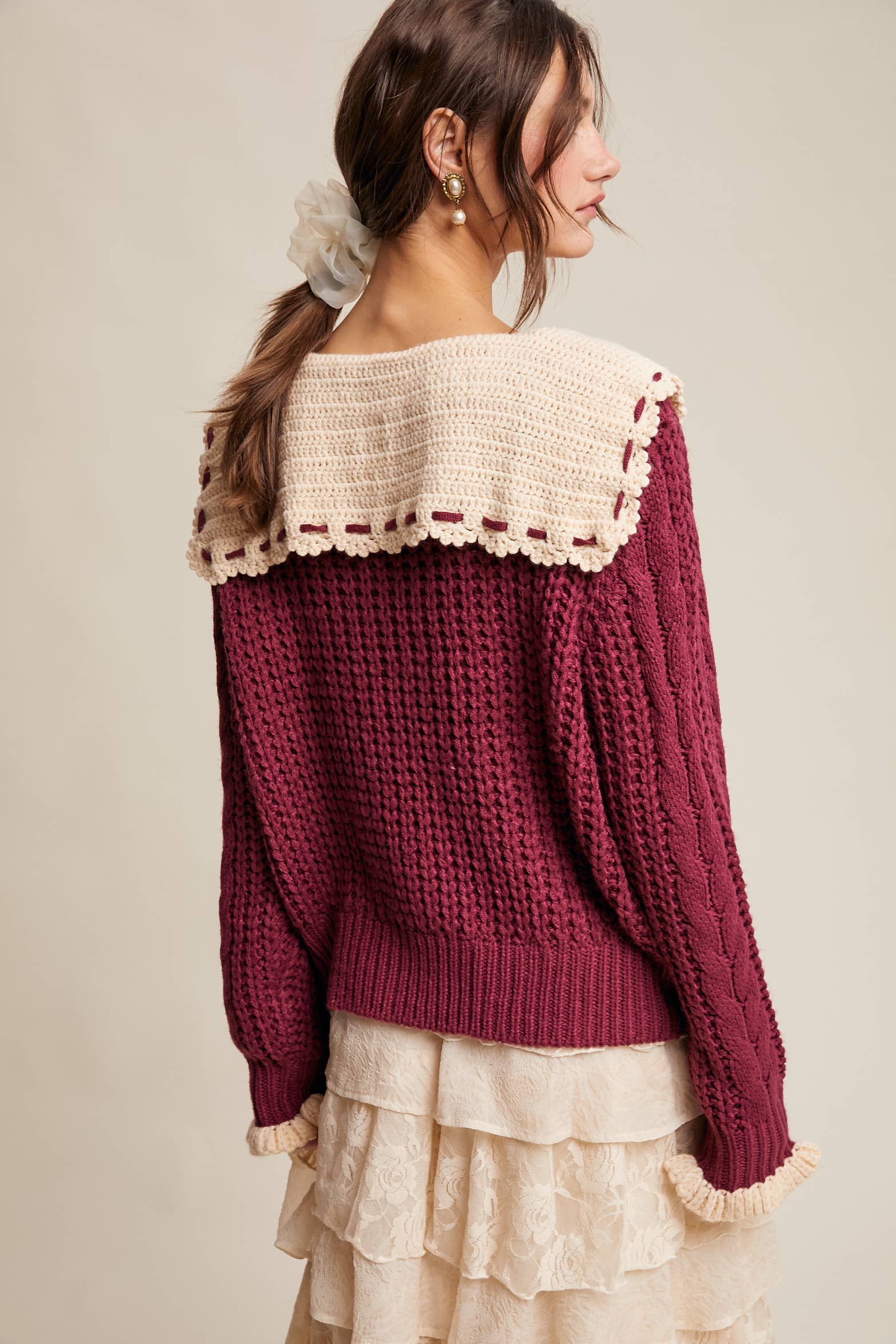 Woman wearing a burgundy sweater with lace details on a beige background