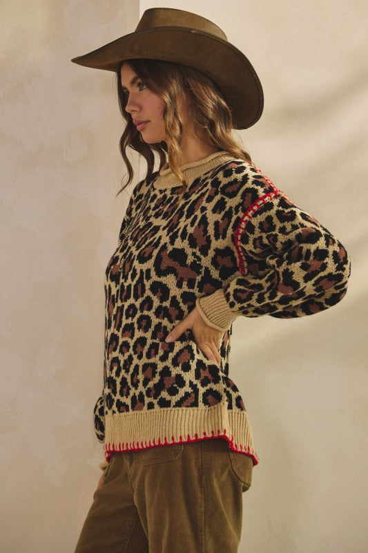 Side view of tan leopard print knit sweater with ribbed crew neck, cuffs and hem plus red whipstitch trim, styled with brown corduroy pants and a cowboy hat.