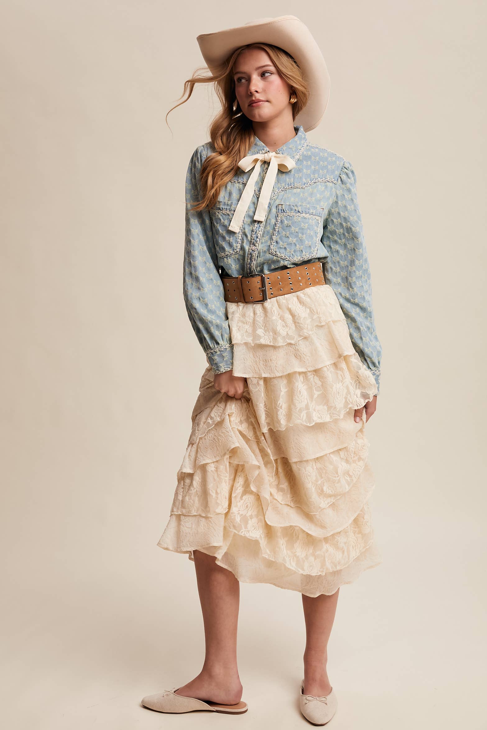 Light-wash denim blouse with cream bow-tie collar, tonal mini-bow pattern, braided contrast stitching, snap front, and two chest pockets.