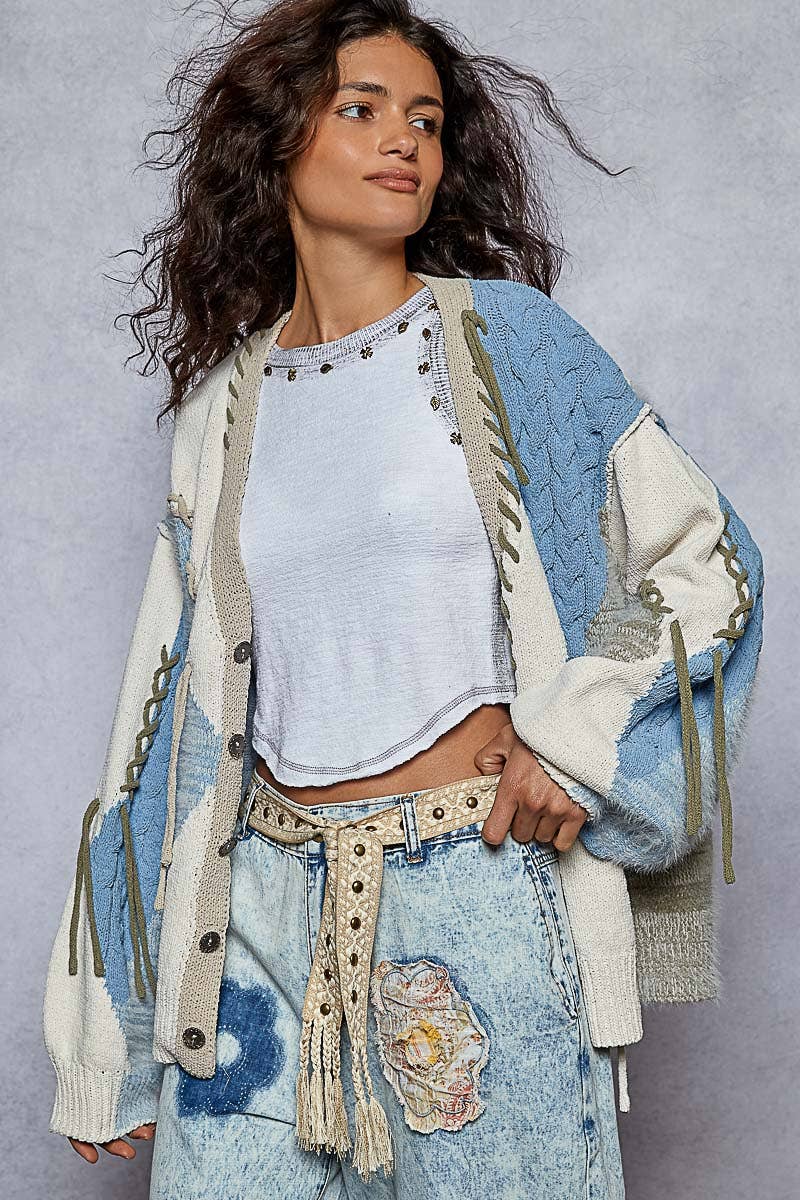 Close-up of a woven black and beige boho belt with stud accents and tassel ends, styled around striped denim jeans with lace patches.