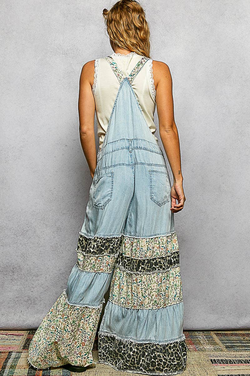 Back view of mixed print ruffle wide leg denim overall — crossed printed straps with lace trim, back pockets, tiered leopard and floral ruffle wide legs