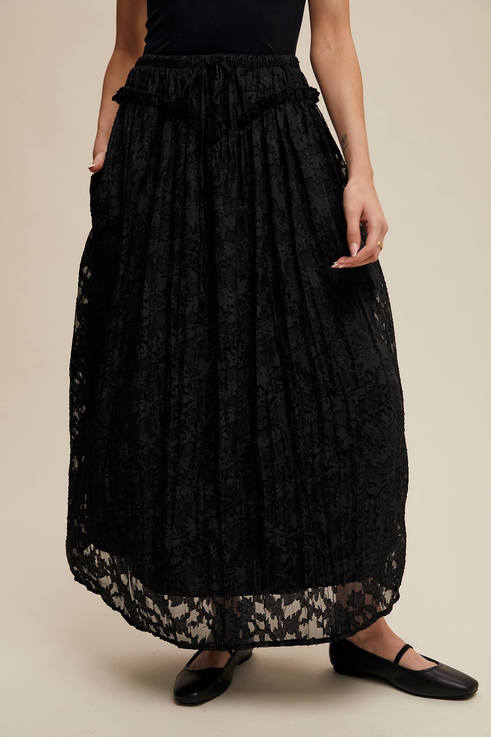 Black floral lace maxi skirt with elastic drawstring waist, ruffle trim and pockets; semi-sheer bubble hem, styled with black Mary Jane flats.