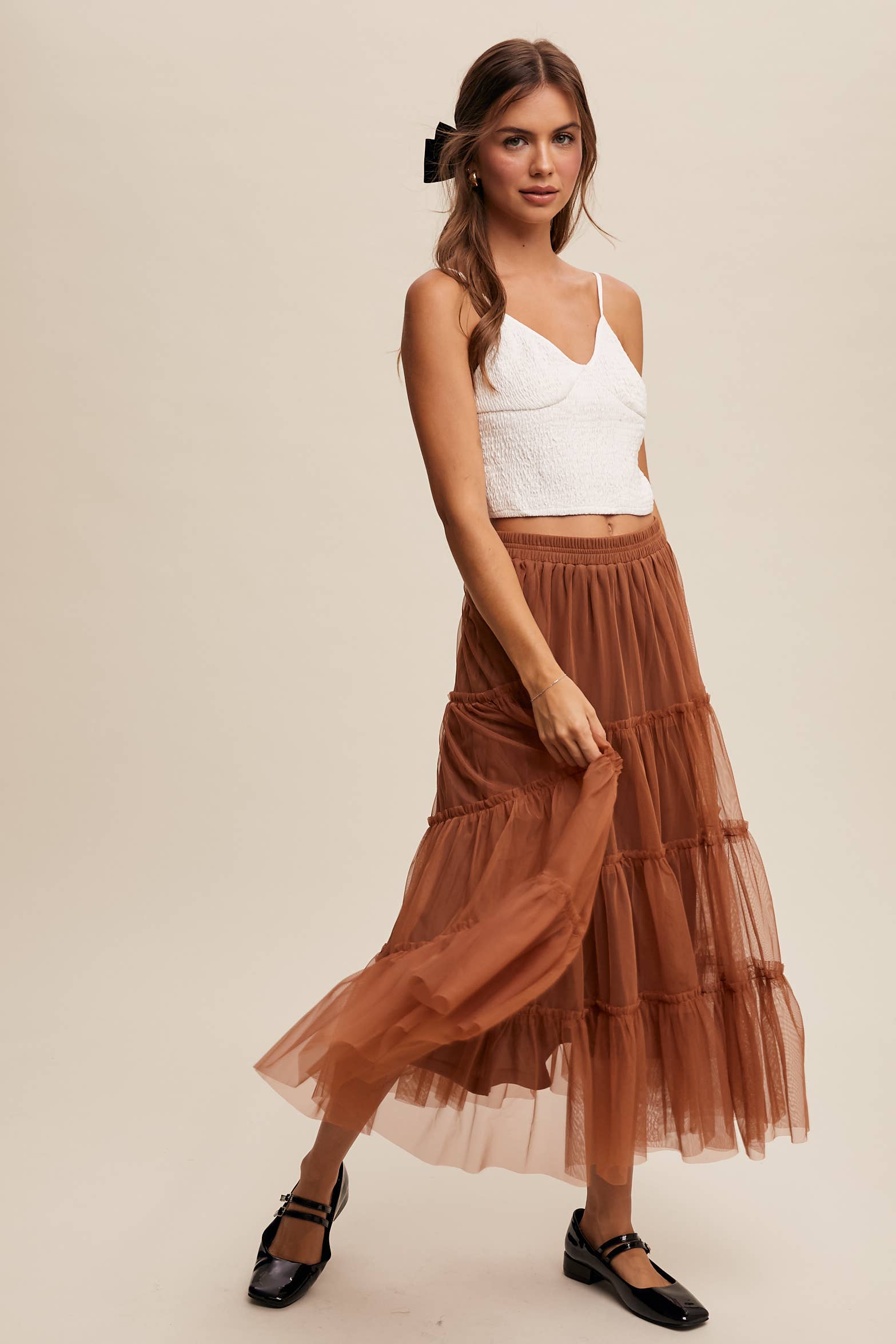 Front view — rust tulle tiered midi skirt with elastic waist and ruffle tiers, sheer overlay; model in black Mary Jane flats.