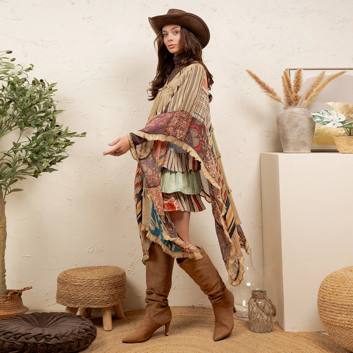 Woman wearing a colorful poncho and brown boots in a home setting with plants and decor.