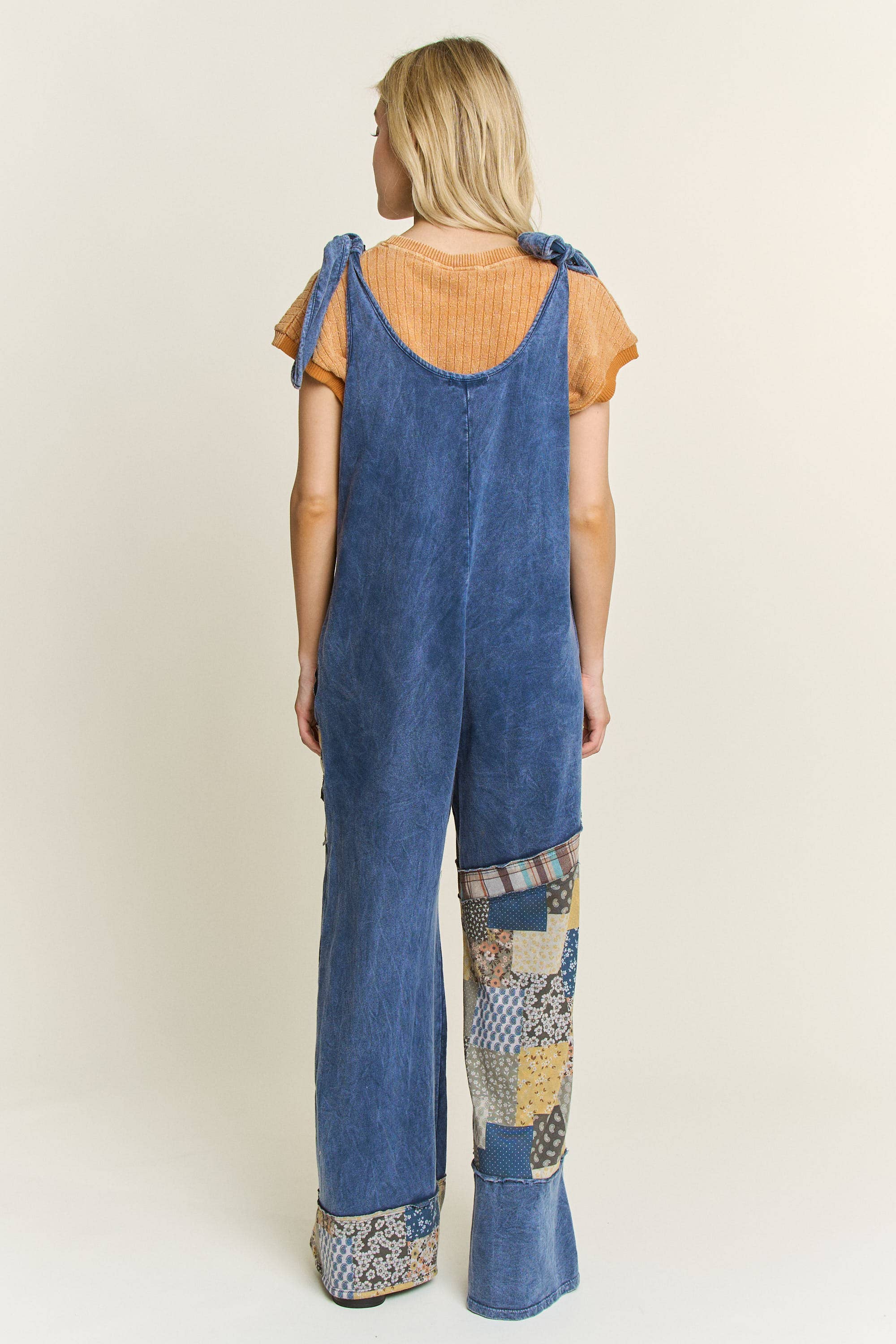 Rear view of woman wearing boho patchwork mineral-wash jumpsuit in navy with daisy appliqués and wide legs.”