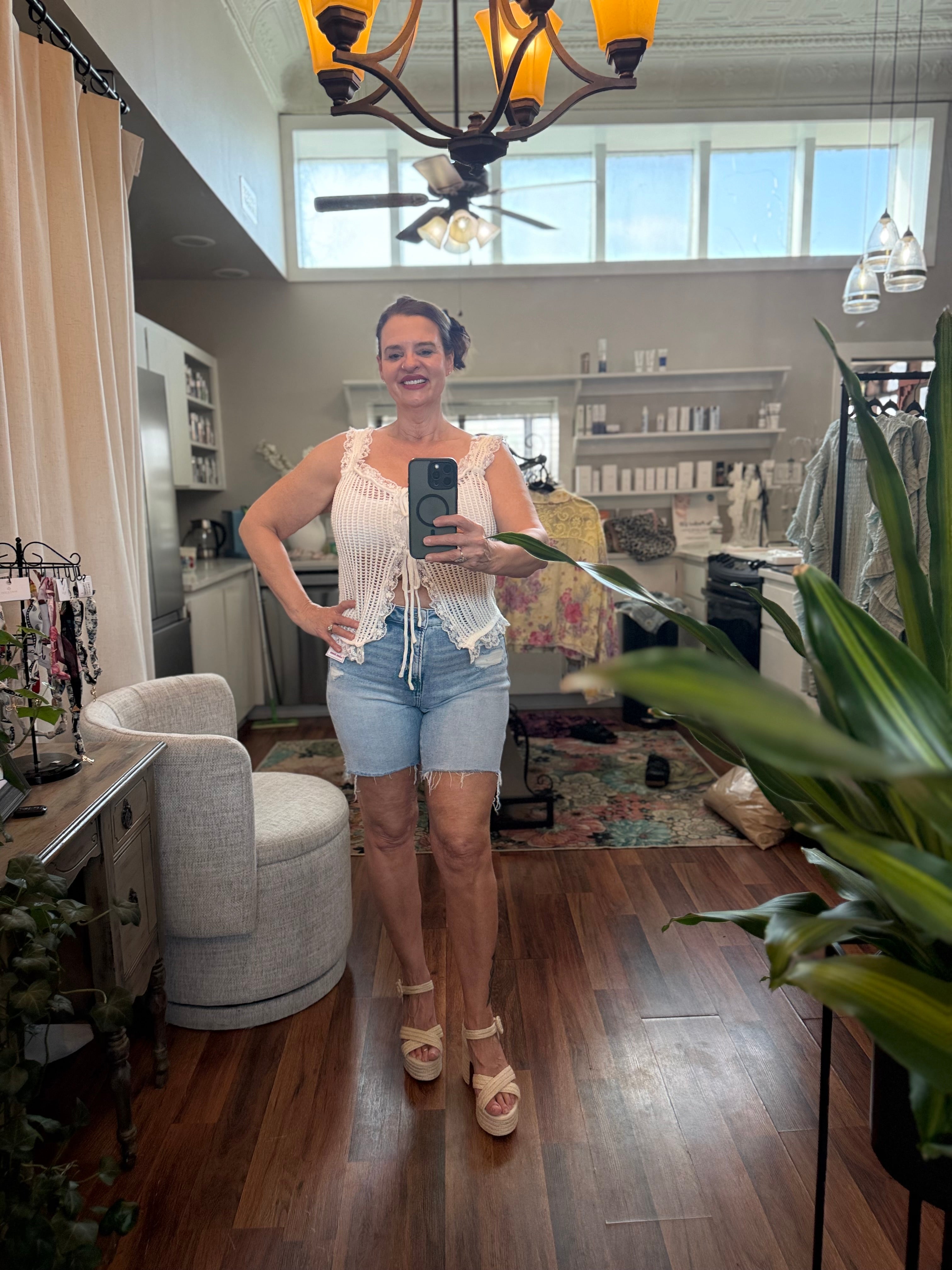 Woman taking a mirror selfie in a living room with a chandelier and plants.