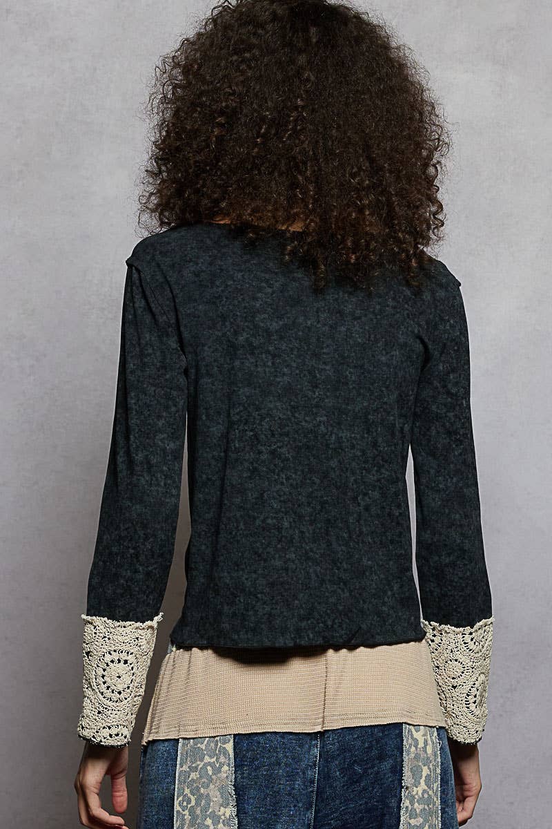 Person wearing a dark gray jacket with lace cuffs and trim on a gray background