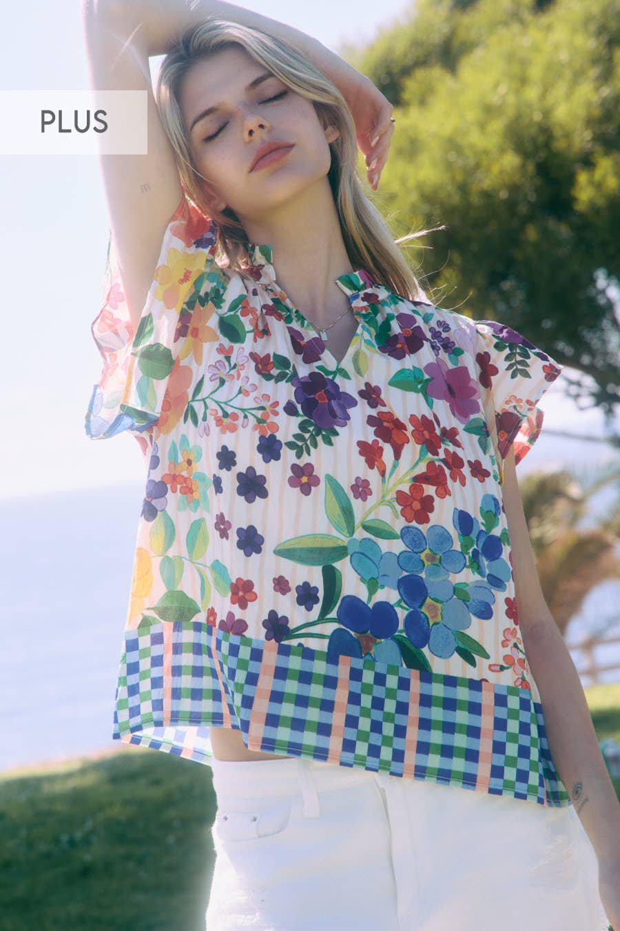 Woman wearing a colorful floral and checkered blouse with trees in the background