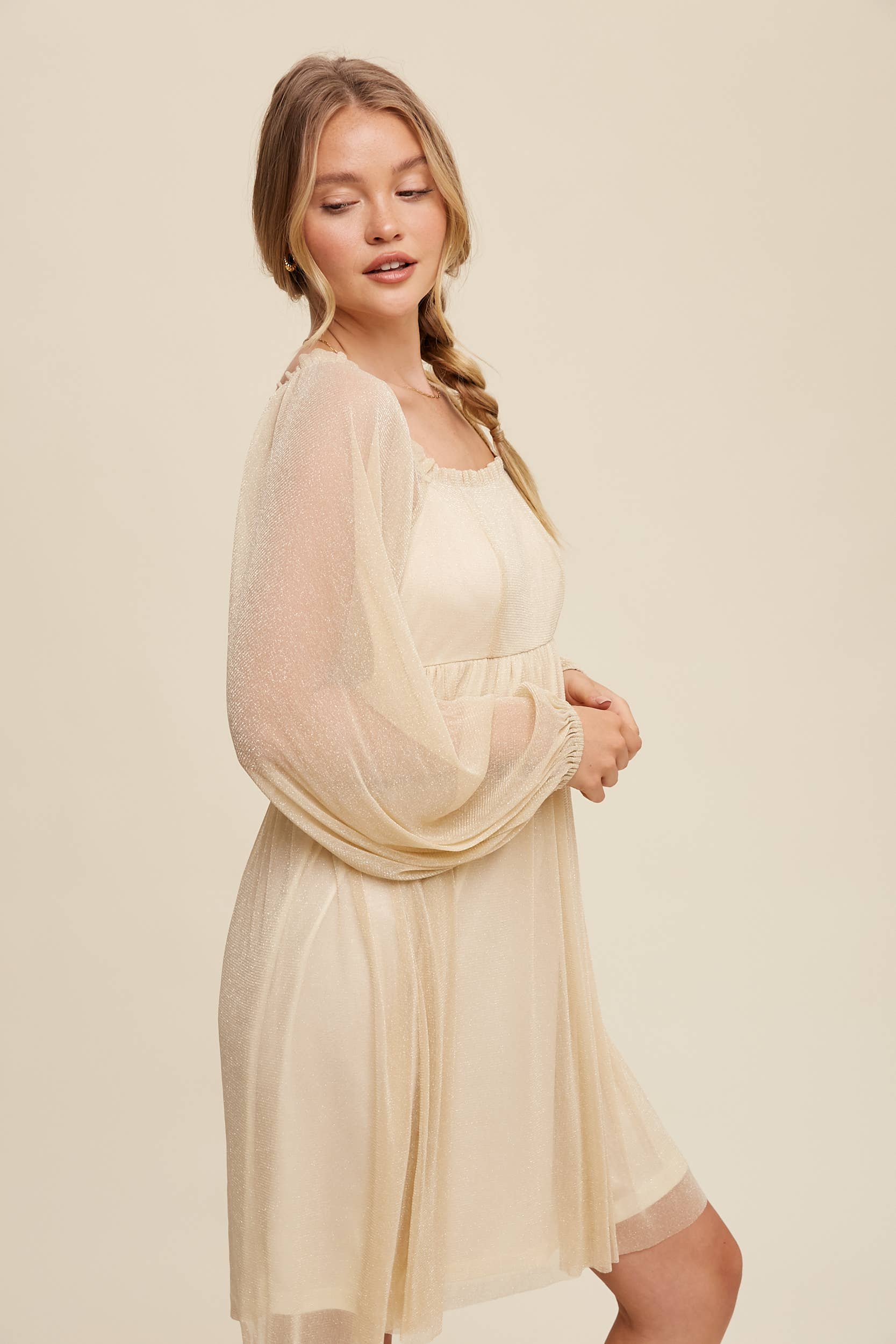 Side view Model wearing a beige shimmer mini dress with long sheer sleeves, square neckline, and flowy A-line silhouette — romantic sparkle party dress
