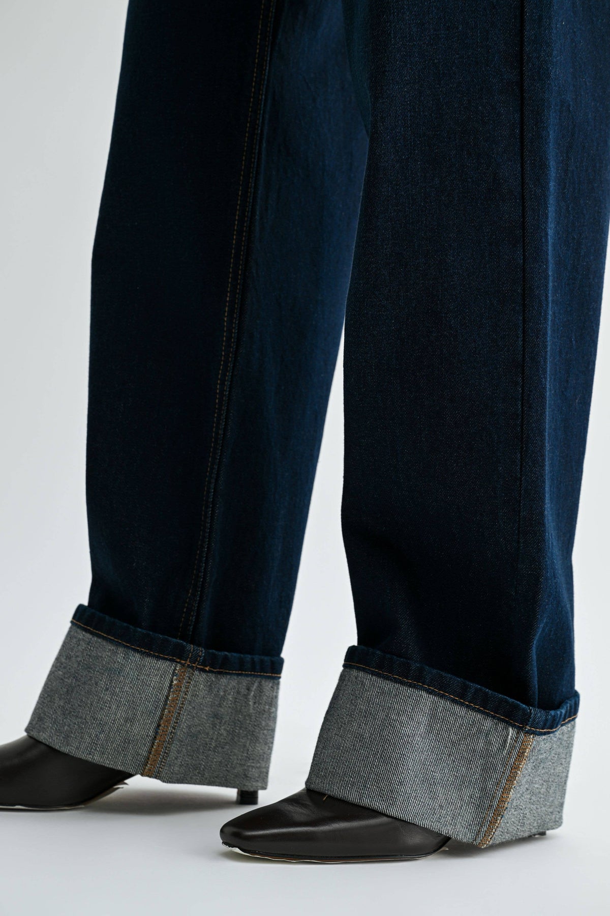 Close-up of the oversized rolled cuffs on Midnight Edge Cuffed Jeans, showing the lighter denim underside over black boots.