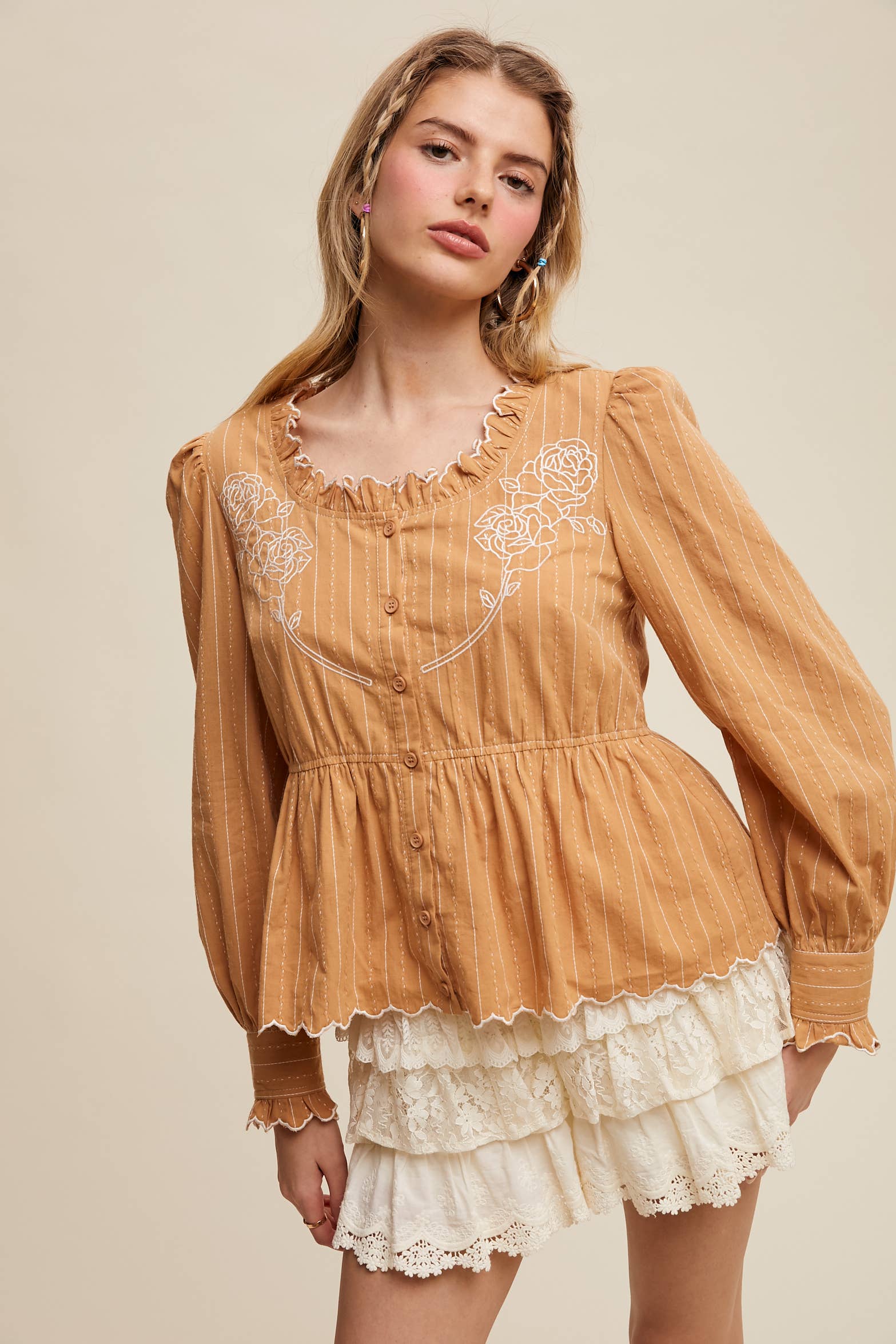 Camel pinstripe blouse with ruffled neckline, white rose embroidery, puff long sleeves, button front, and scalloped peplum hem—styled with white lace shorts.