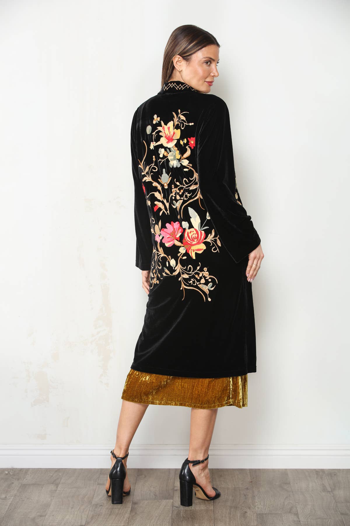 Back view of black velvet duster with large pink, red and cream floral embroidery, styled with a gold dress.