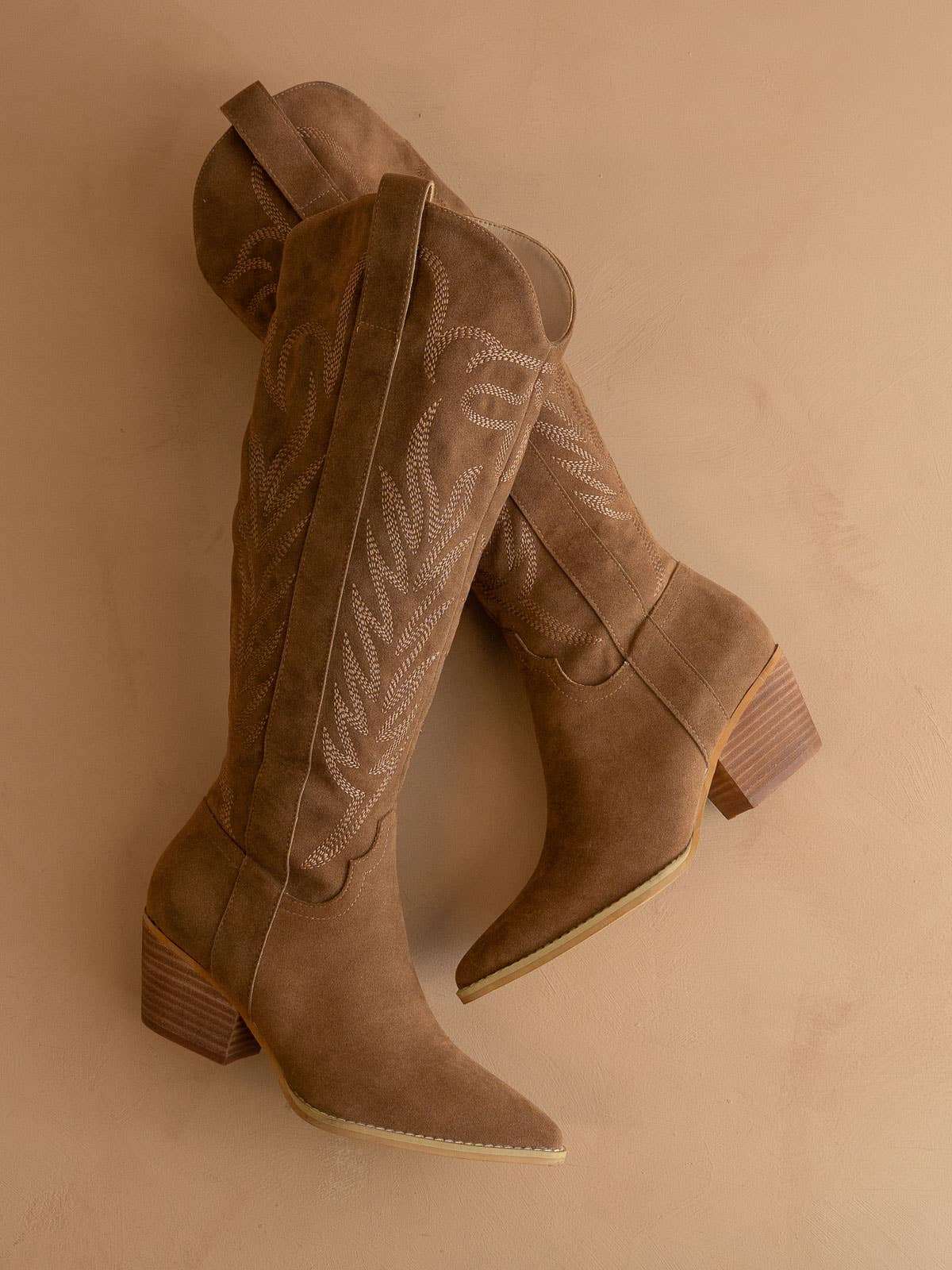 Taupe suede knee-high western boot with stitched shaft, pull tab, pointed toe, and stacked block heel, side view.
