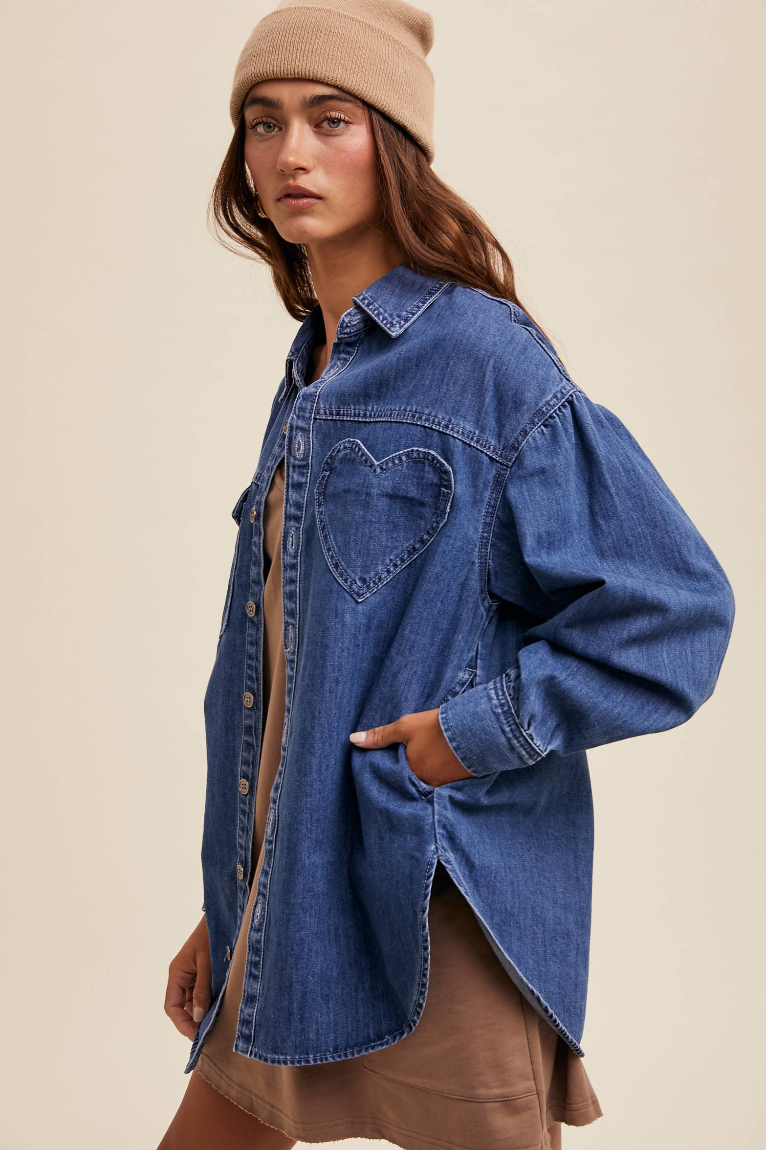 Side view- Medium-wash oversized denim shacket with button front, drop shoulders, balloon sleeves, side pockets, and a curved shirttail hem with side slits.