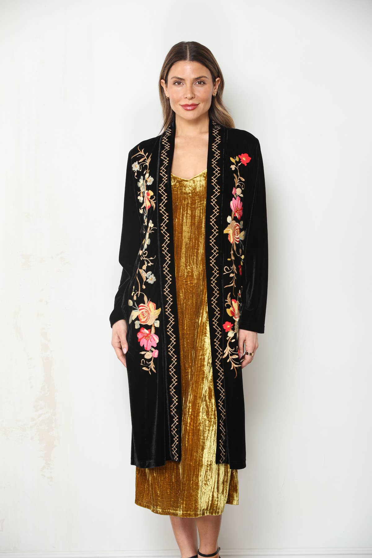 Front view of Paparazzi black velvet duster with colorful floral embroidery and stitched trim over a gold dress.