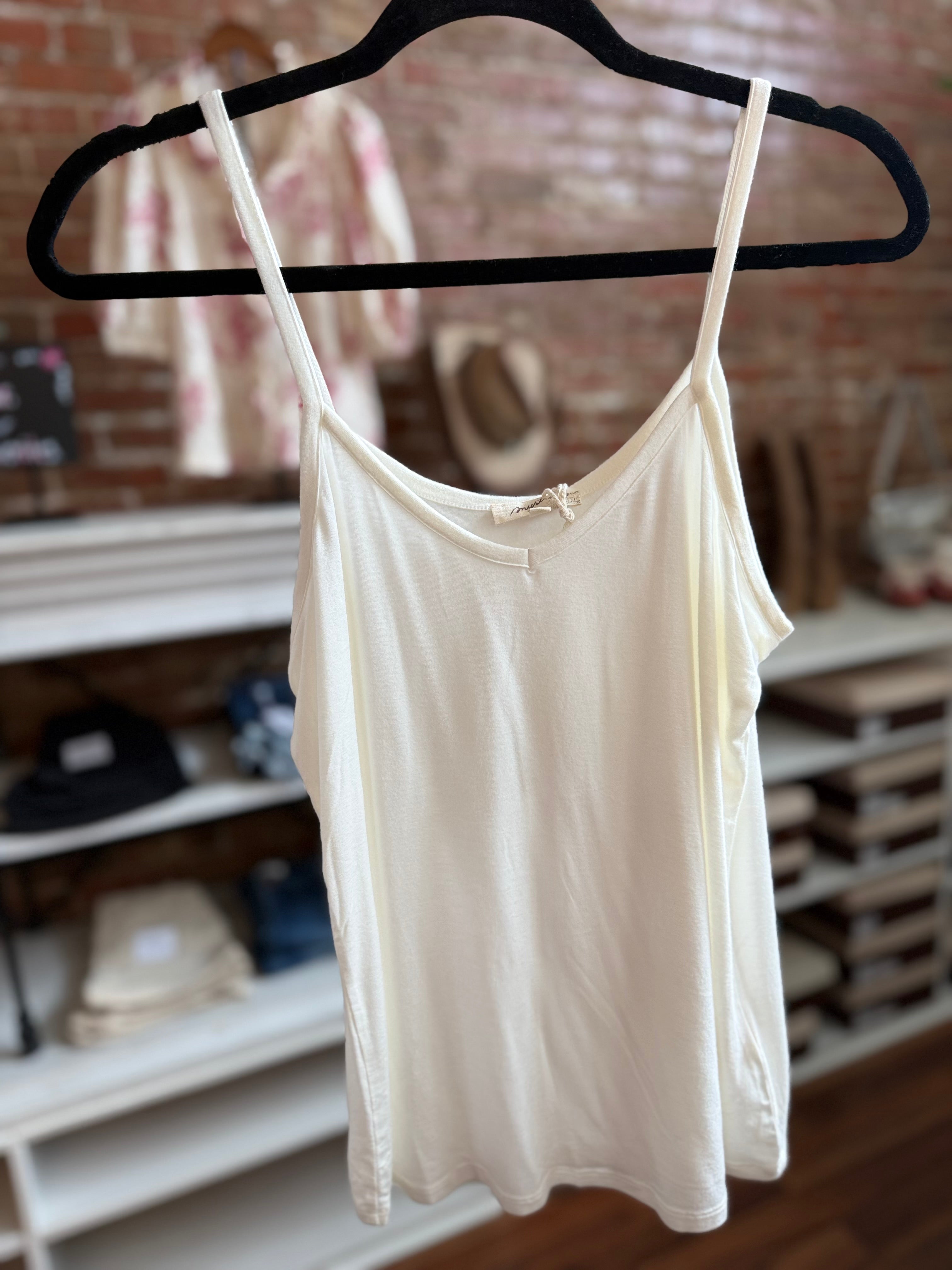 White tank top on a black hanger against a blurred indoor background