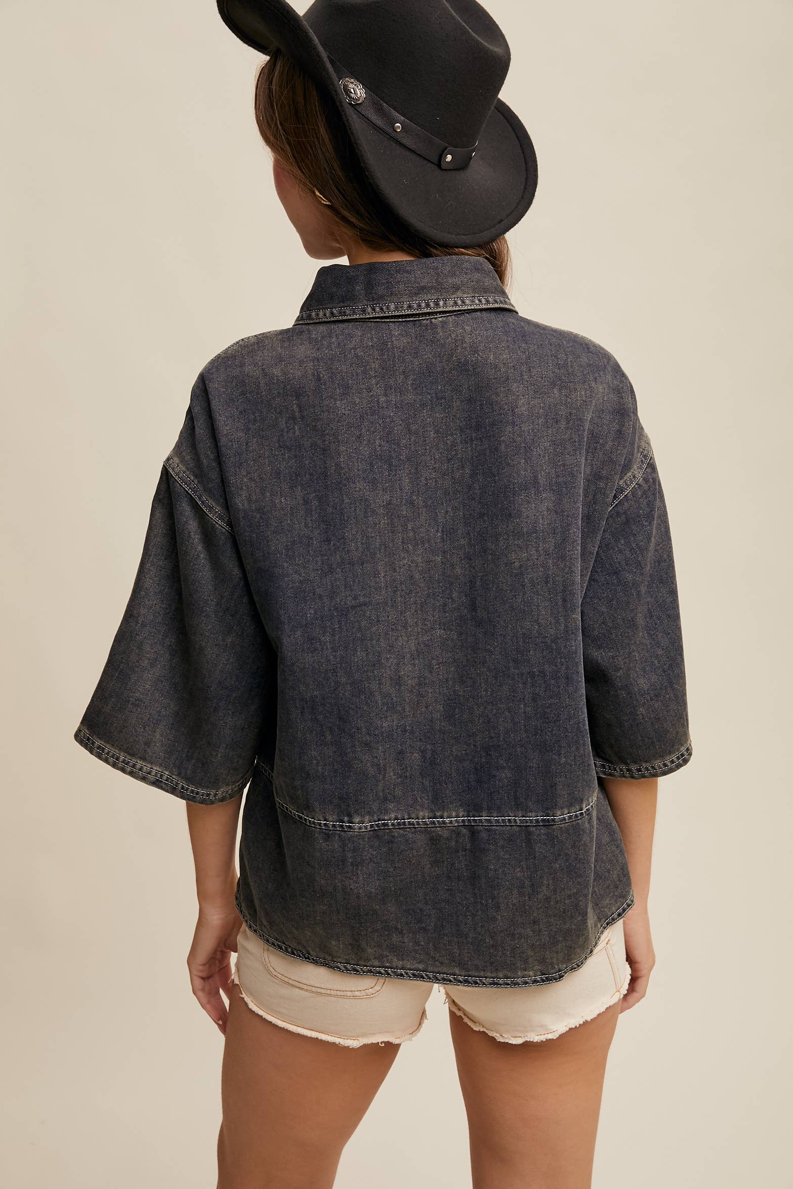 Back view- Dark-wash denim pullover top with half-button placket, exposed seam panels, and wide elbow-length sleeves in a relaxed, boxy fit.