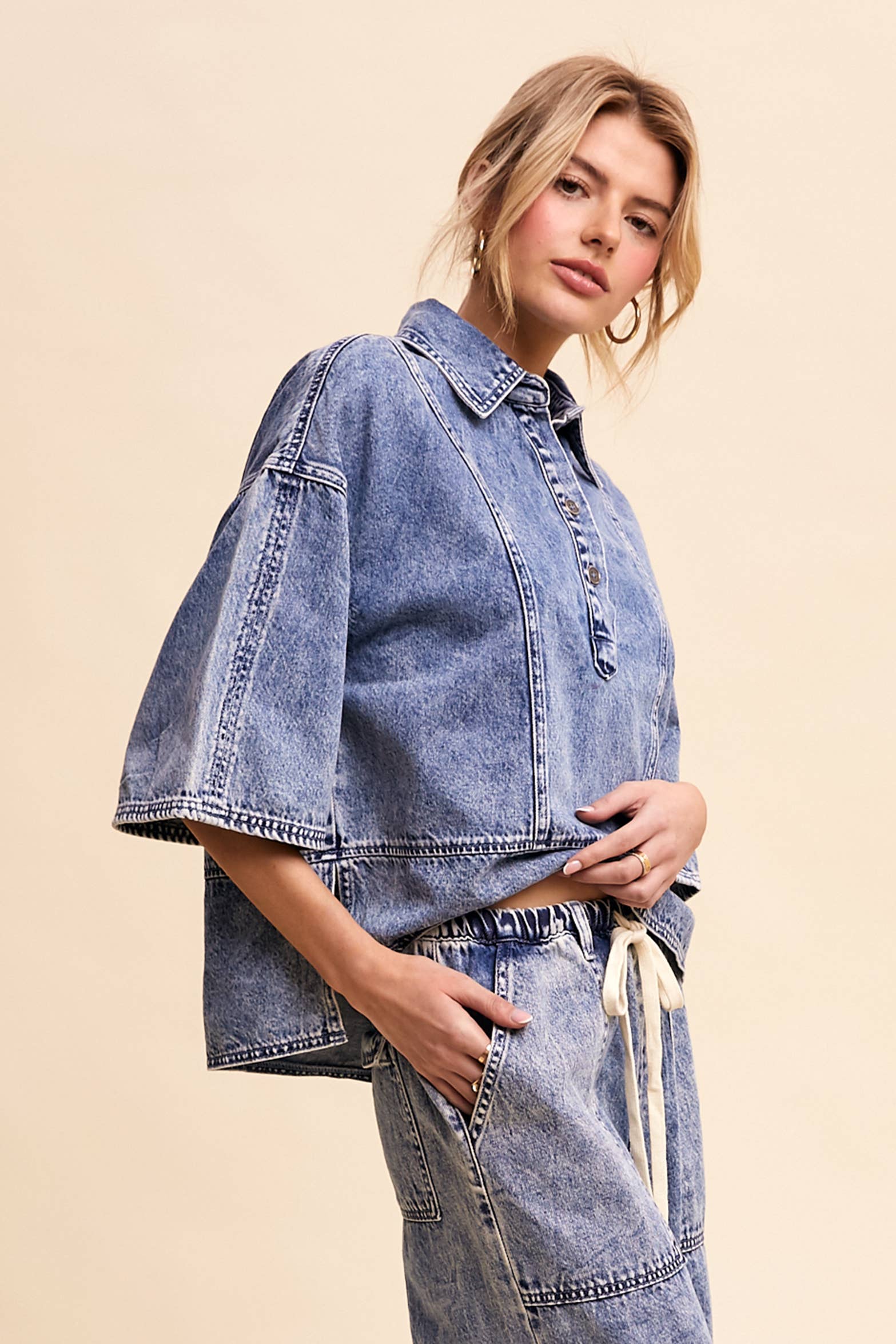 Side view- Light-wash denim pullover top with a half-button placket, exposed seam panels, and wide elbow-length sleeves in a relaxed, boxy fit.