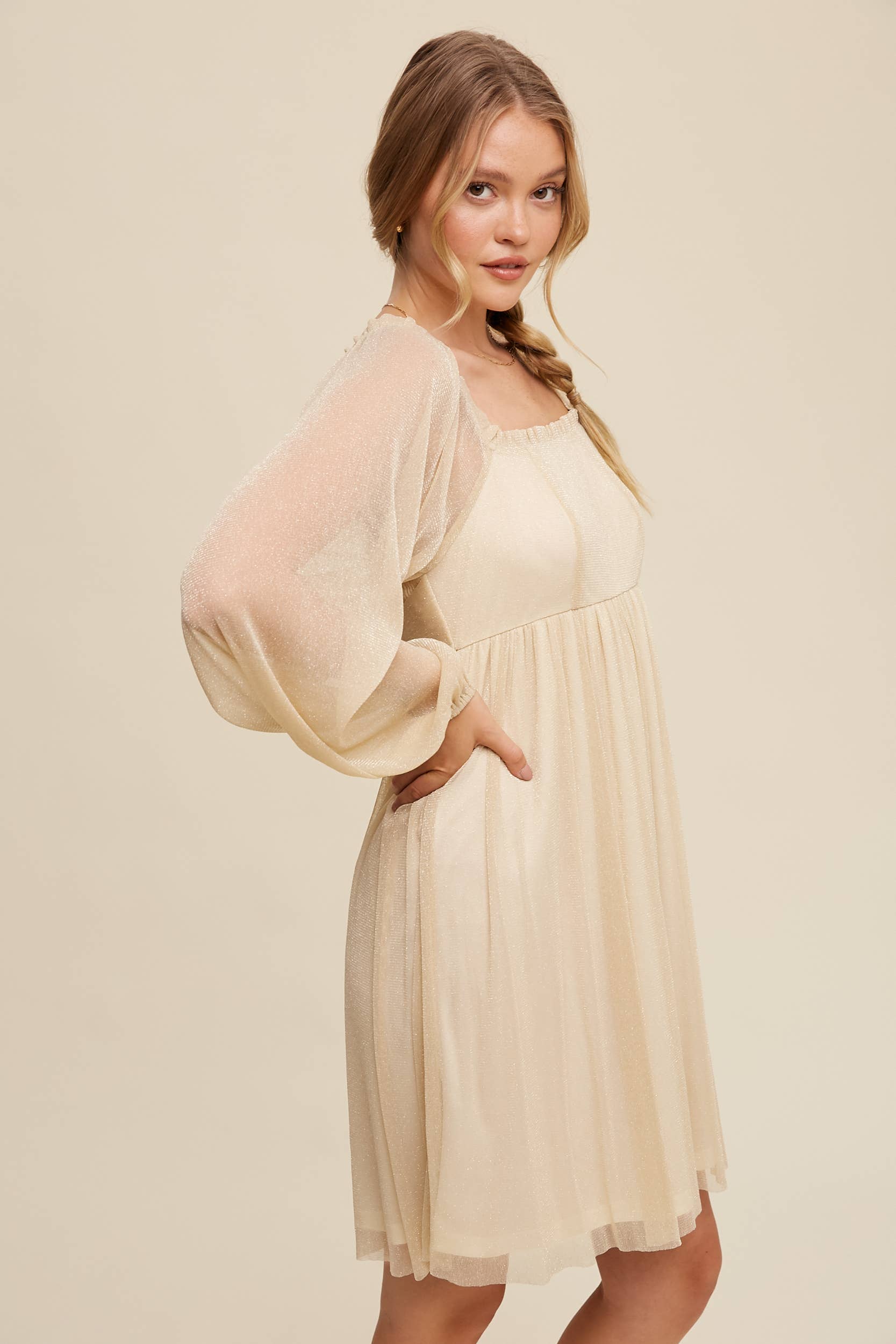 Side view Model wearing a beige shimmer mini dress with long sheer sleeves, square neckline, and flowy A-line silhouette — romantic sparkle party dress
