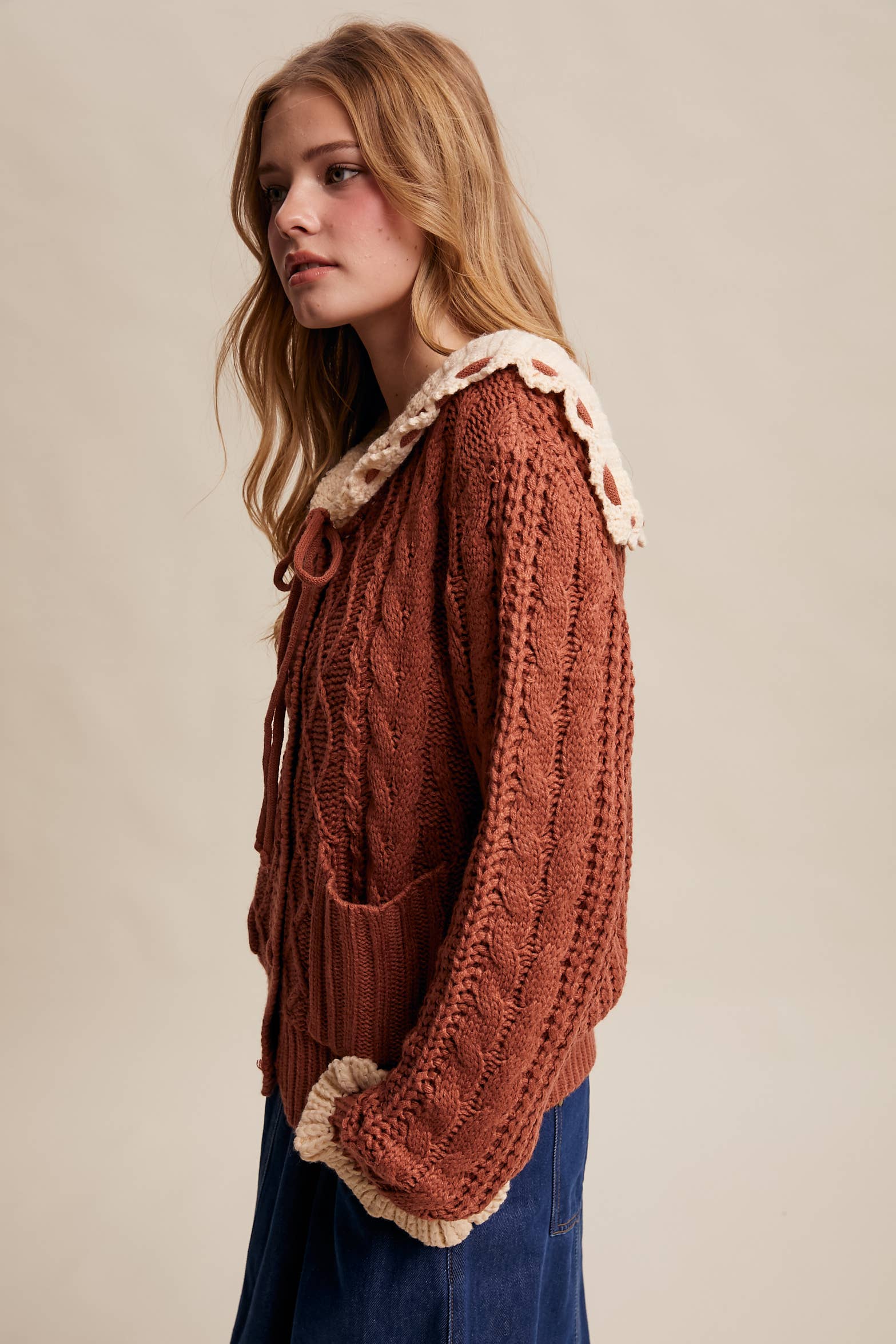 Woman wearing a brown knitted sweater with white trim on a beige background