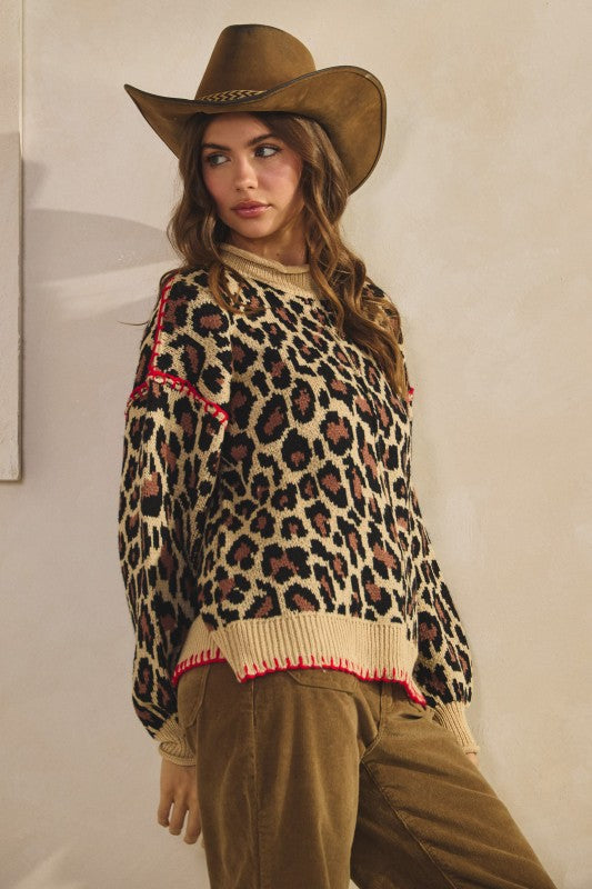 Side view of tan leopard print knit sweater with ribbed crew neck, cuffs and hem plus red whipstitch trim, styled with brown corduroy pants and a cowboy hat.