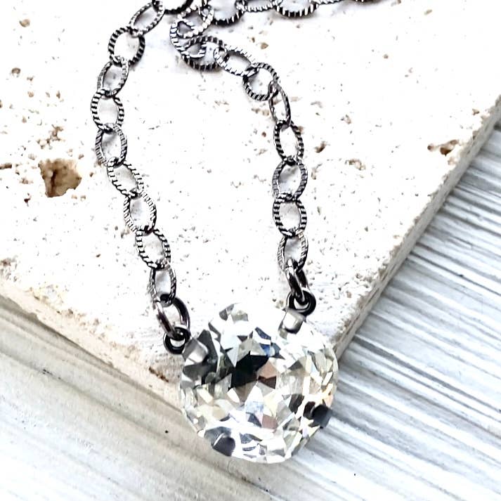 Silver chain necklace with a clear crystal pendant on a textured surface