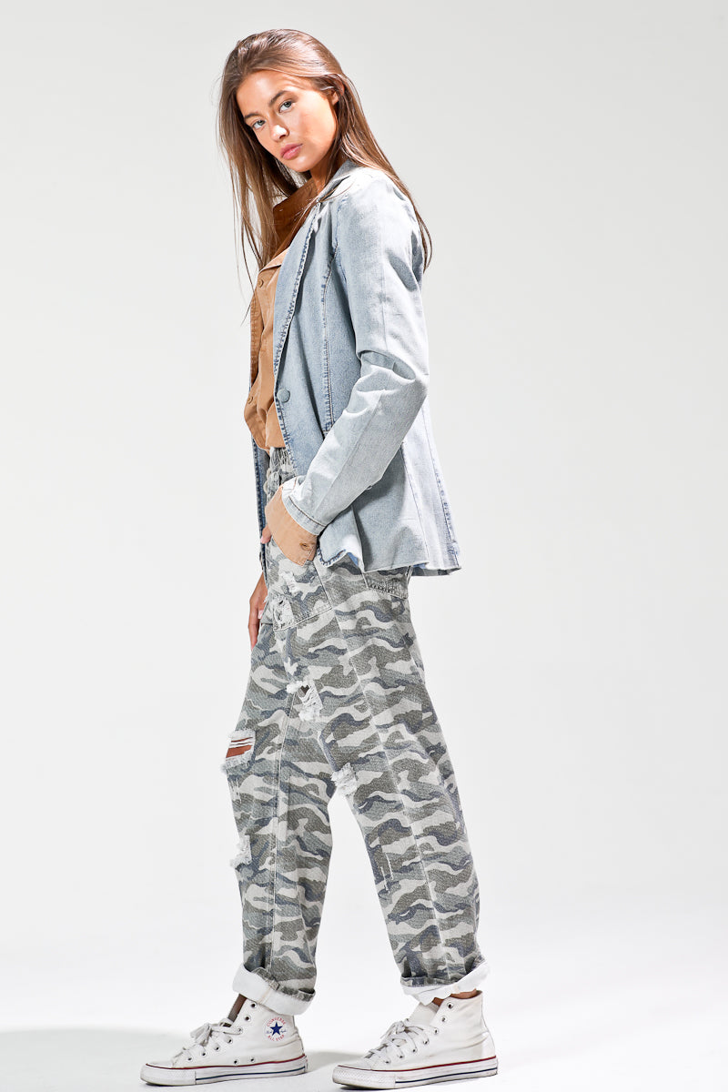 Side profile of model wearing light-wash denim blazer layered over tan shirt with camo pants and sneakers.