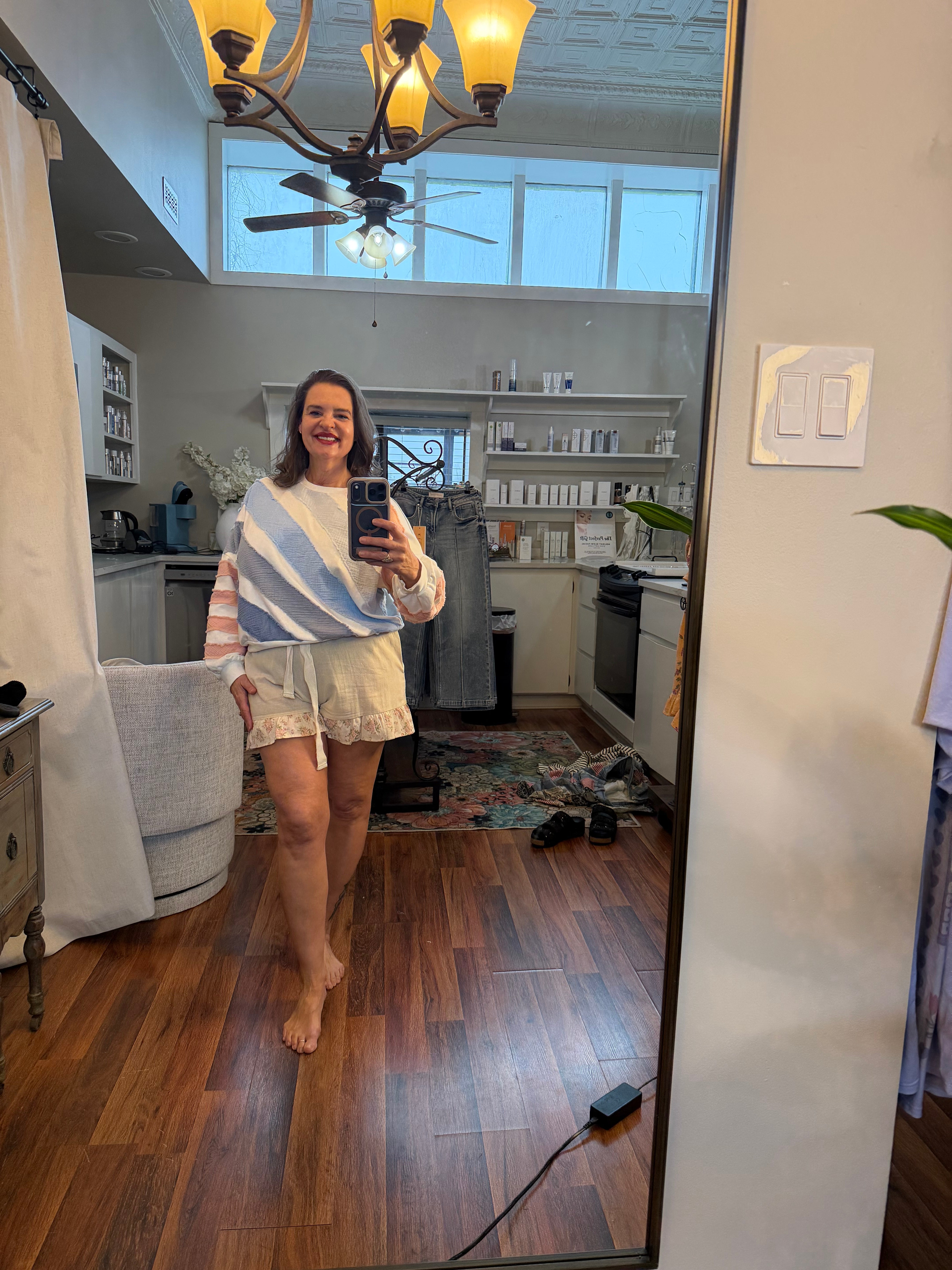 Person standing in a room with wooden floor and white walls, holding a phone.