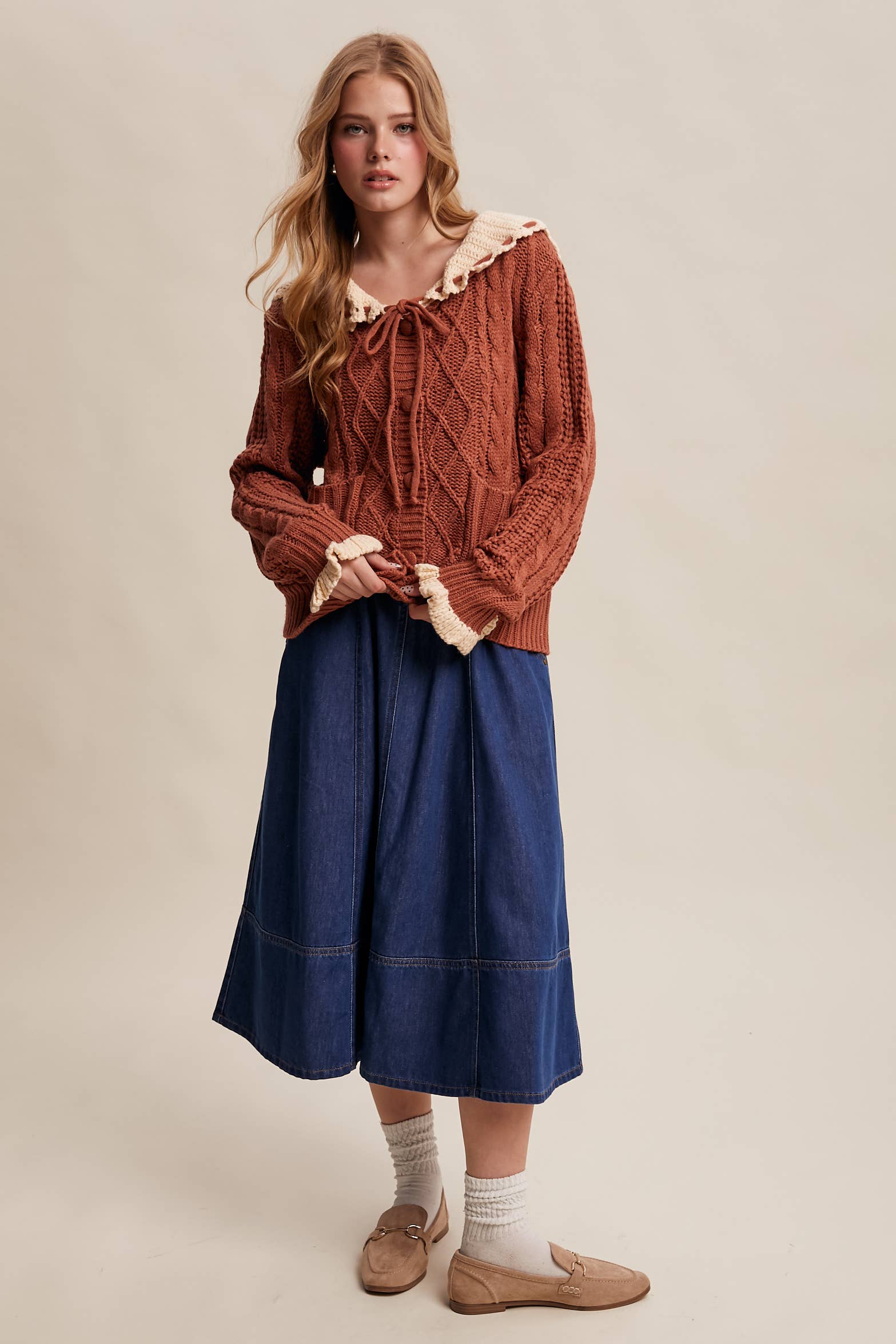 Woman wearing a brown cable knit sweater and blue skirt on a beige background