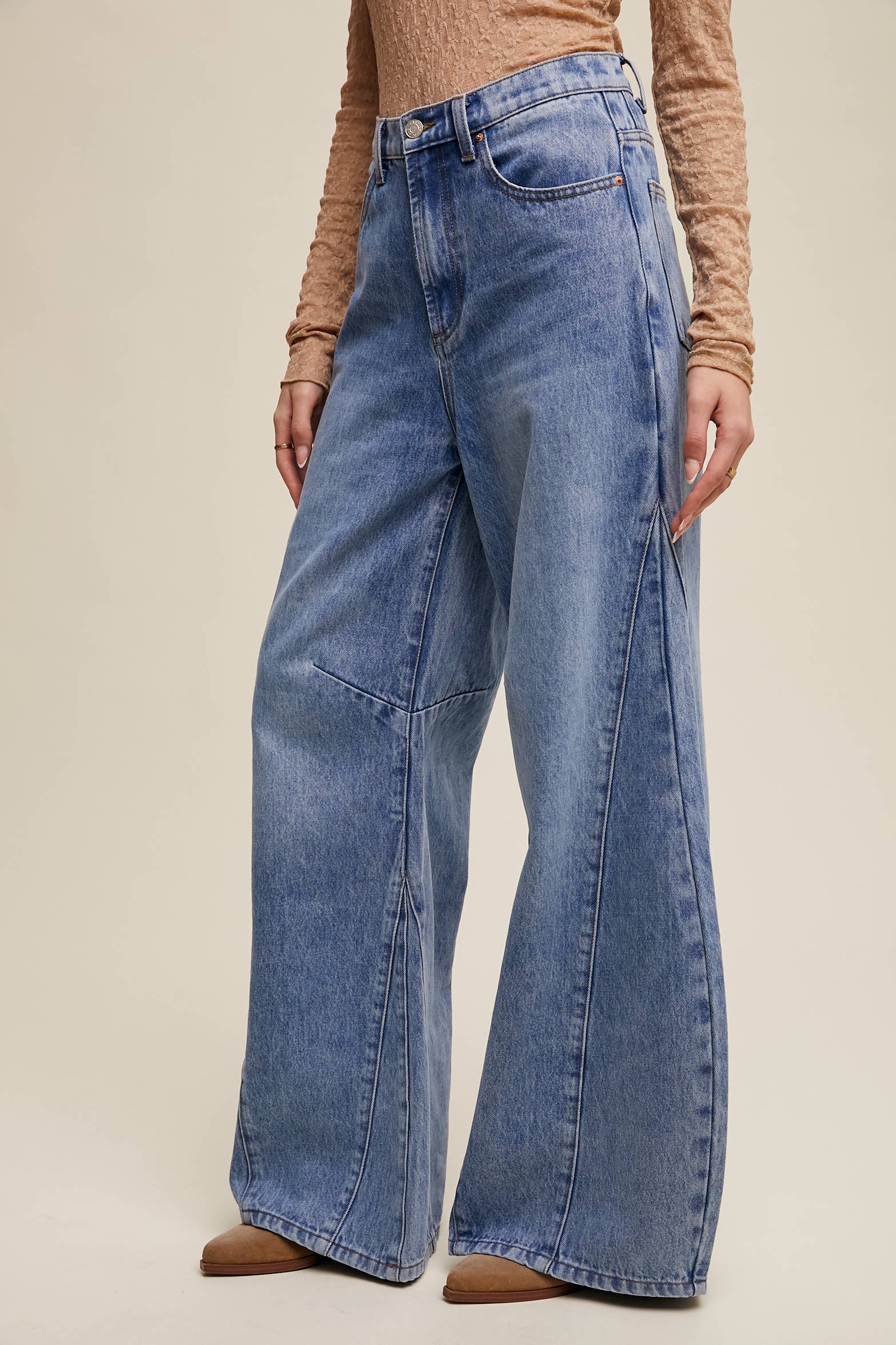Side view- High-rise light-wash wide-leg jeans with front seam panels and knee darts, five-pocket style with zip fly, styled with tan long-sleeve top and pointed-toe boots.